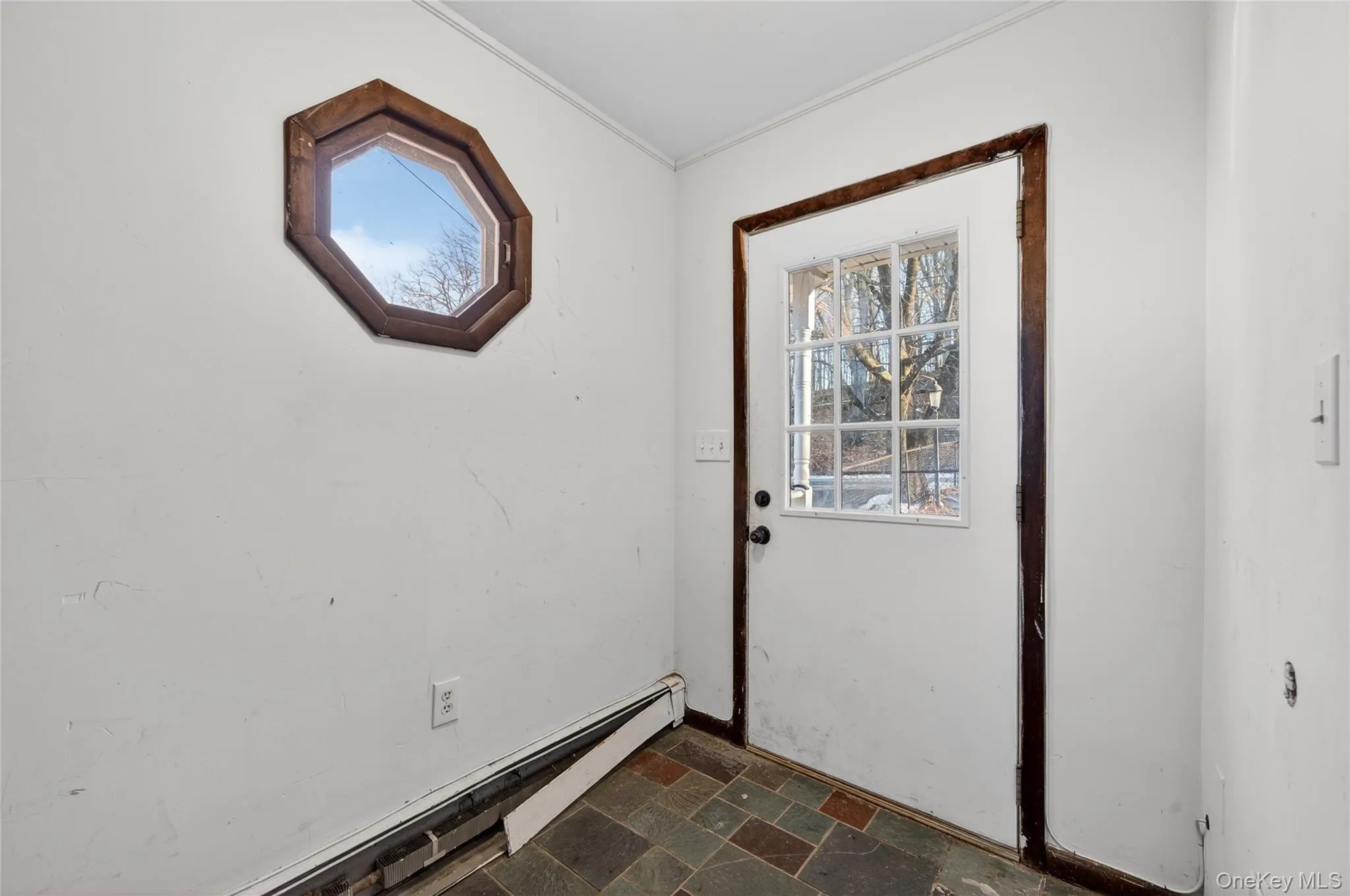 Doorway featuring stone tile flooring, a baseboard heating unit, and crown molding Doorway featuring stone tile flooring, a baseboard heating unit, and crown molding
