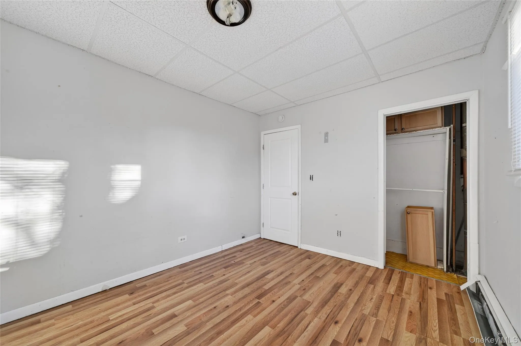 Unfurnished bedroom featuring a paneled ceiling, baseboard heating, and light wood-style flooring Unfurnished bedroom featuring a paneled ceiling, baseboard heating, and light wood-style flooring