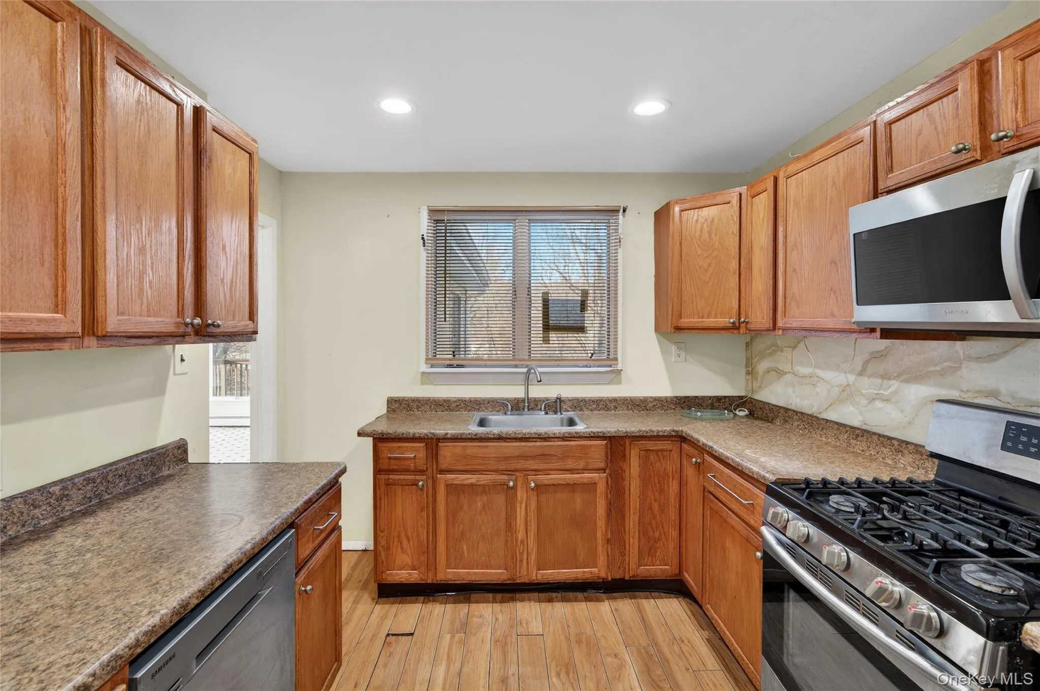Kitchen with stainless steel appliances, light wood-type flooring, recessed lighting, decorative backsplash, and dark countertops Kitchen with stainless steel appliances, light wood-type flooring, recessed lighting, decorative backsplash, and dark countertops