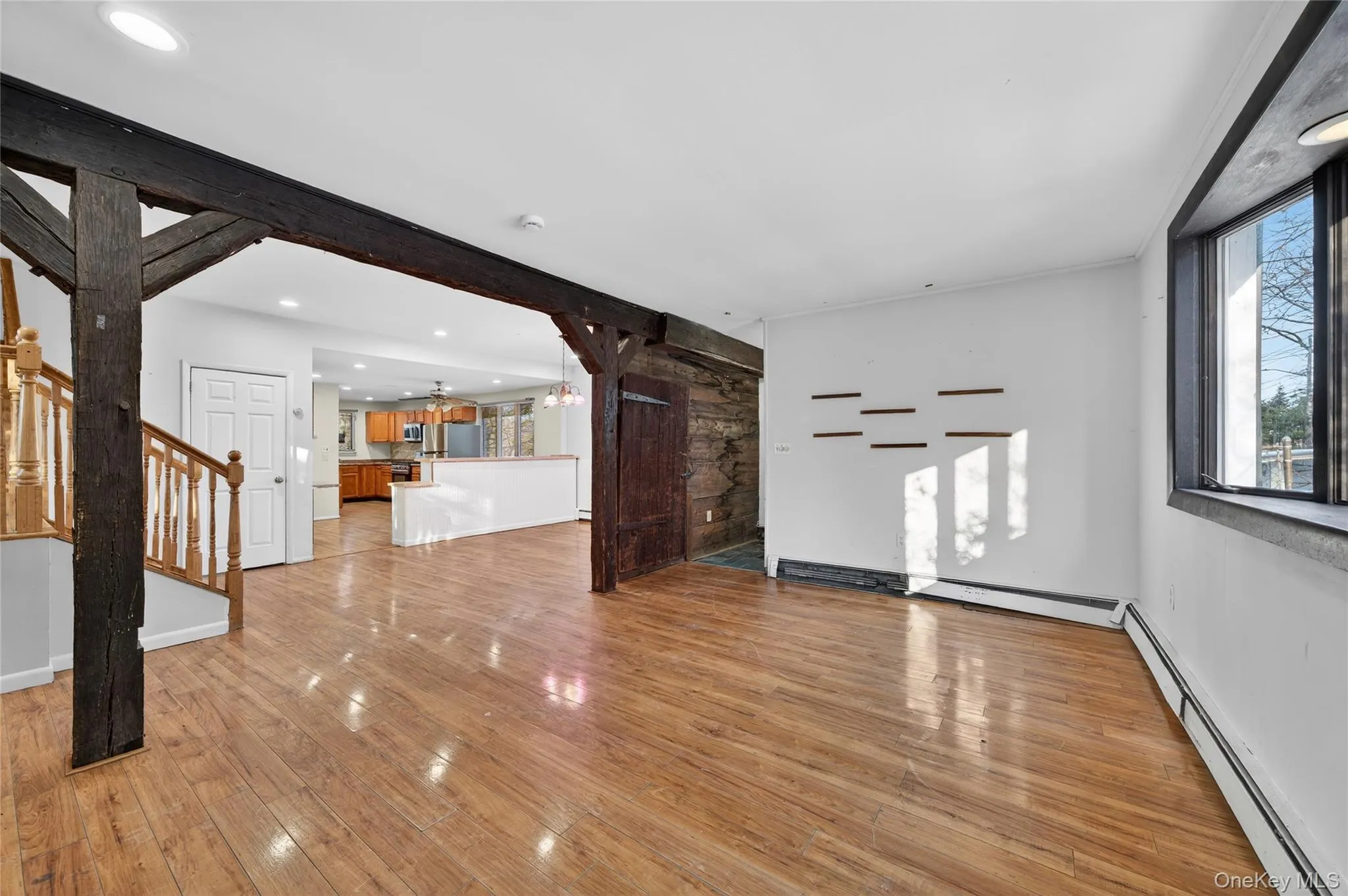 Unfurnished living room with a baseboard heating unit, stairway, and light wood finished floors Unfurnished living room with a baseboard heating unit, stairway, and light wood finished floors