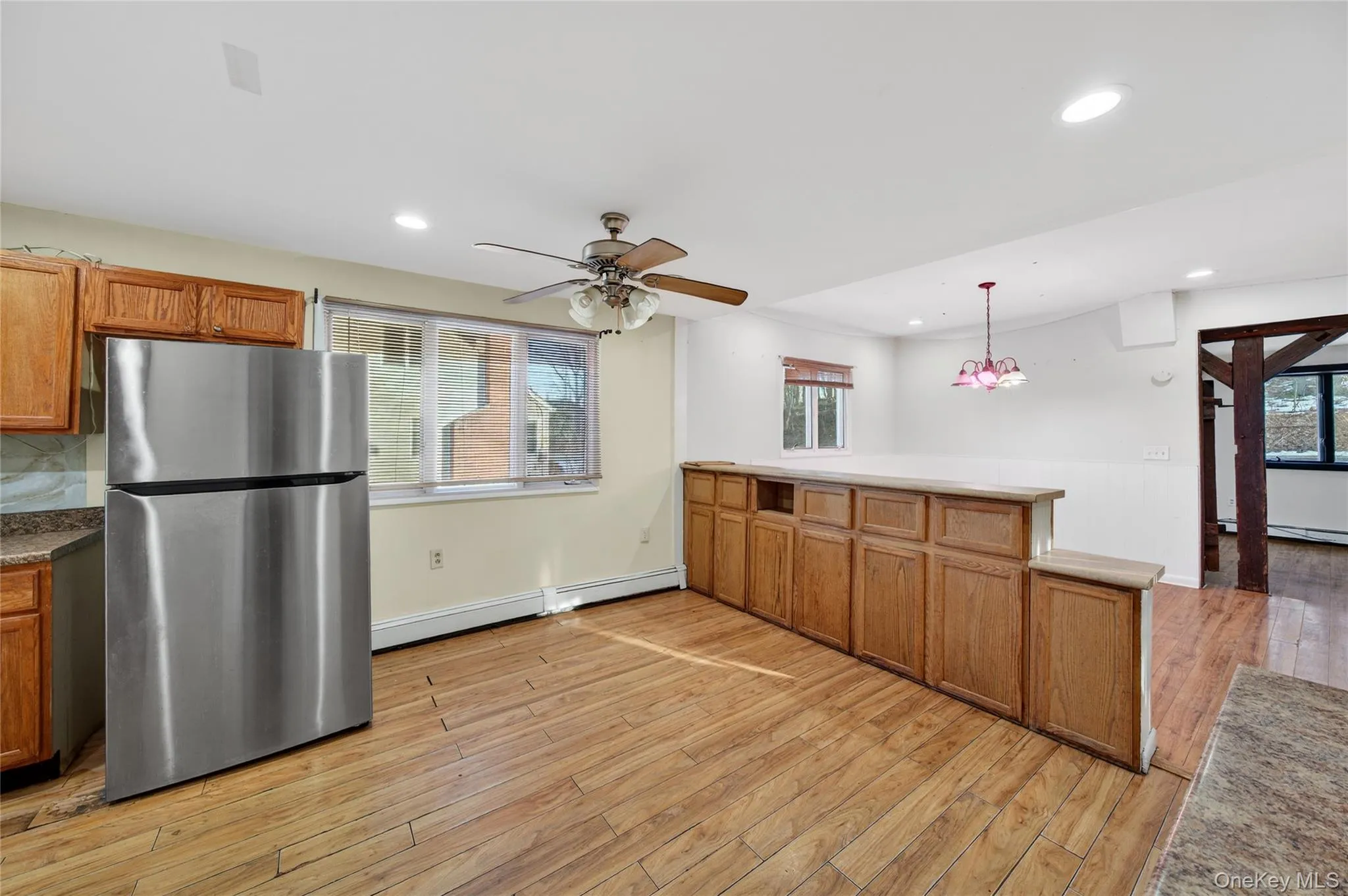 Kitchen featuring brown cabinets, freestanding refrigerator, a peninsula, pendant lighting, and light wood finished floors Kitchen featuring brown cabinets, freestanding refrigerator, a peninsula, pendant lighting, and light wood finished floors