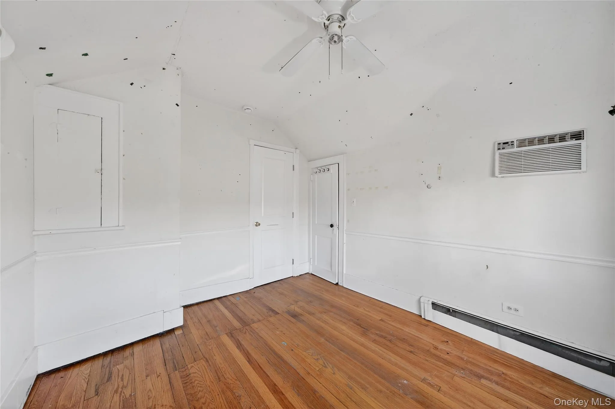 Spare room featuring baseboard heating, lofted ceiling, hardwood / wood-style flooring, ceiling fan, and an AC wall unit Spare room featuring baseboard heating, lofted ceiling, hardwood / wood-style flooring, ceiling fan, and an AC wall unit