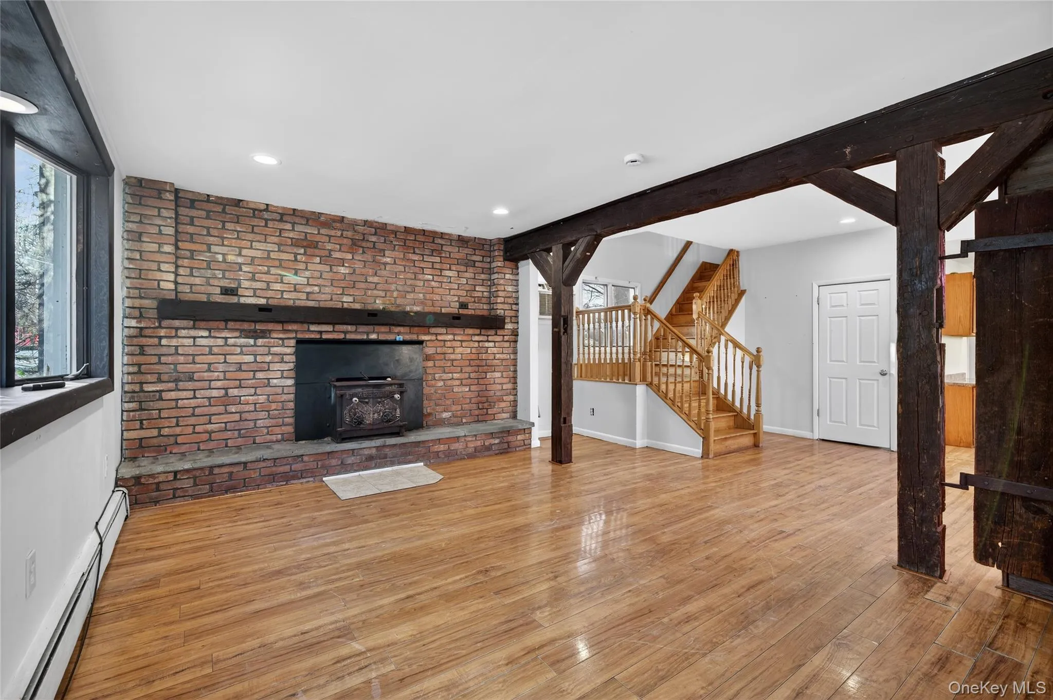 Unfurnished living room with a baseboard heating unit, hardwood / wood-style flooring, stairway, recessed lighting, and beam ceiling Unfurnished living room with a baseboard heating unit, hardwood / wood-style flooring, stairway, recessed lighting, and beam ceiling