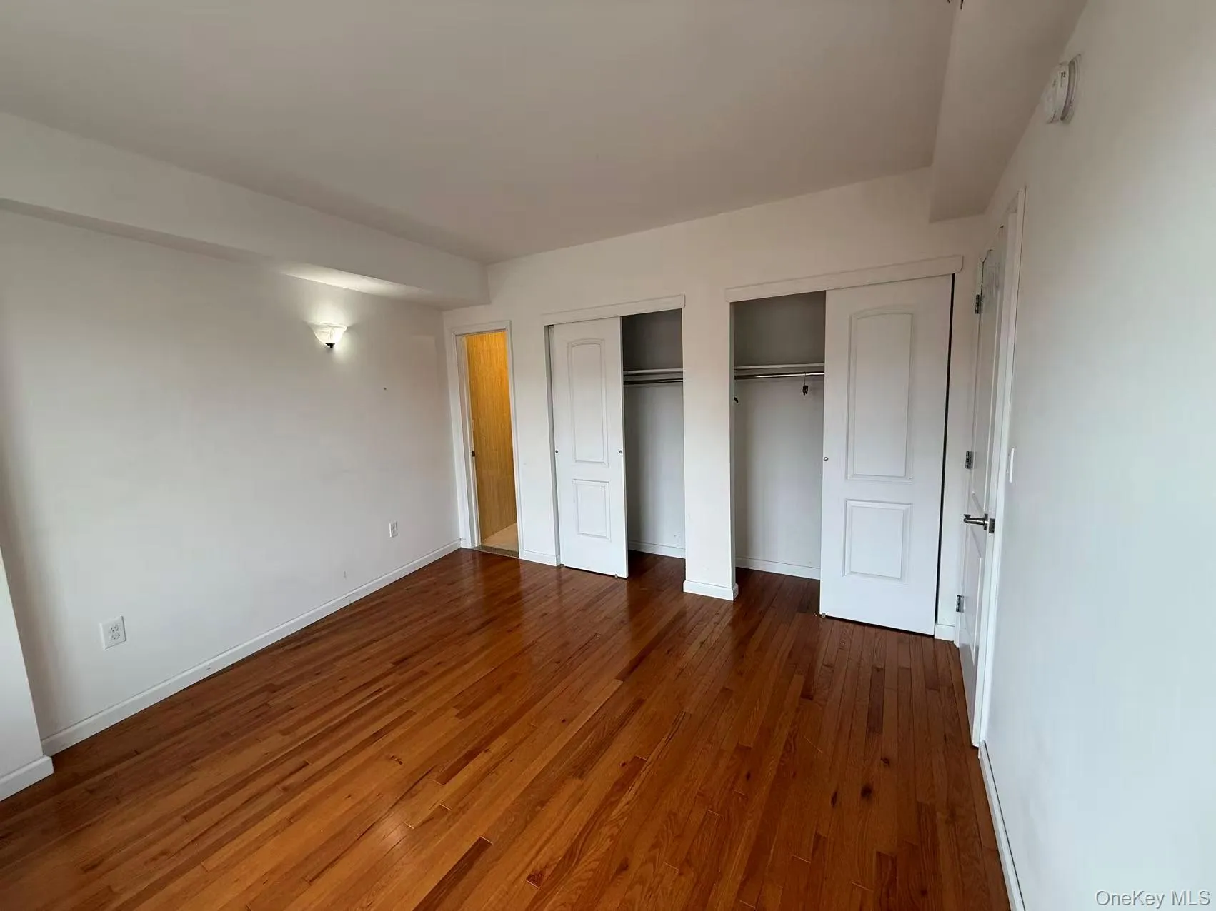 Unfurnished bedroom with multiple closets and dark wood-type flooring Unfurnished bedroom with multiple closets and dark wood-type flooring