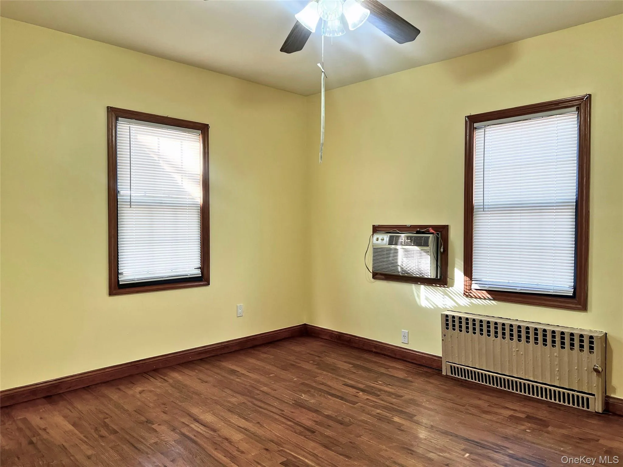 Unfurnished room featuring radiator heating unit, dark wood-type flooring, and a wall mounted air conditioner Unfurnished room featuring radiator heating unit, dark wood-type flooring, and a wall mounted air conditioner