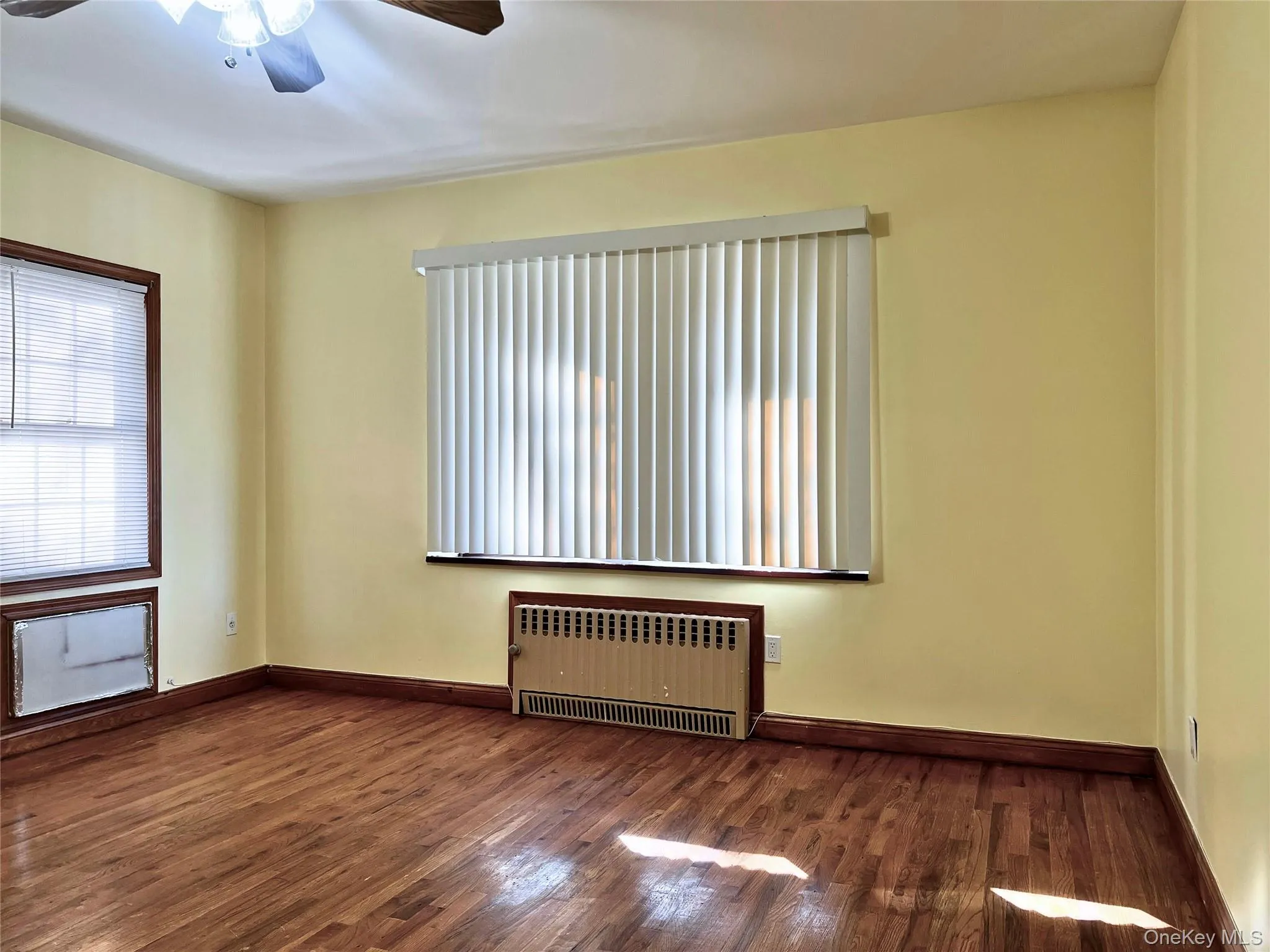Spare room with radiator heating unit, a ceiling fan, and dark wood-type flooring Spare room with radiator heating unit, a ceiling fan, and dark wood-type flooring