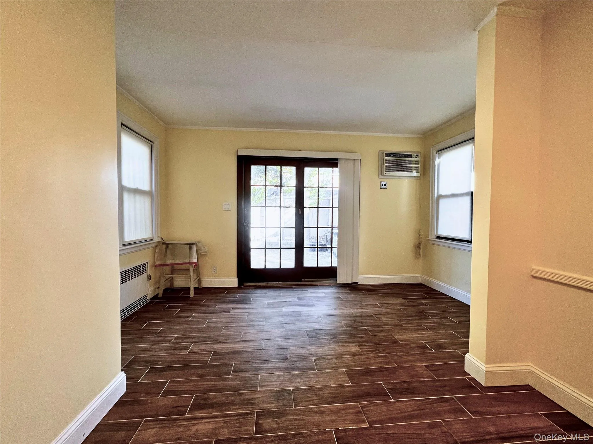 Doorway to outside featuring wood finish floors, radiator, ornamental molding, and an AC wall unit Doorway to outside featuring wood finish floors, radiator, ornamental molding, and an AC wall unit