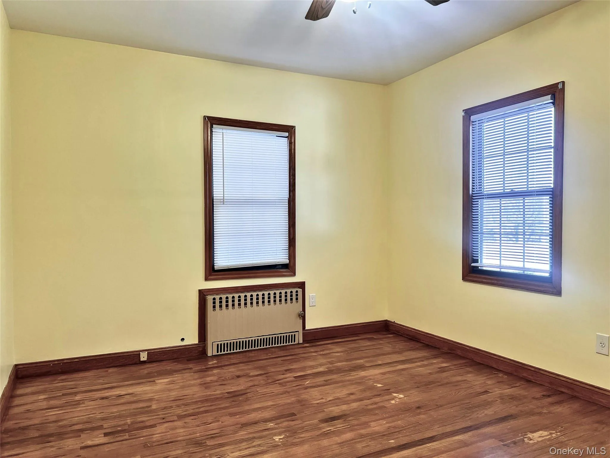 Unfurnished room with radiator, dark wood finished floors, and a ceiling fan Unfurnished room with radiator, dark wood finished floors, and a ceiling fan