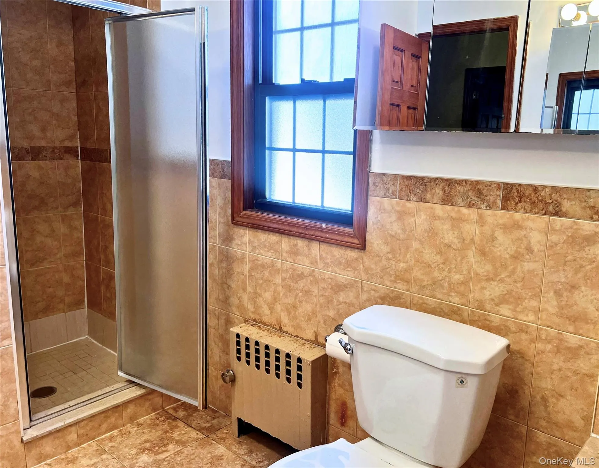 Full bath featuring radiator, a stall shower, tile walls, and a wainscoted wall Full bath featuring radiator, a stall shower, tile walls, and a wainscoted wall