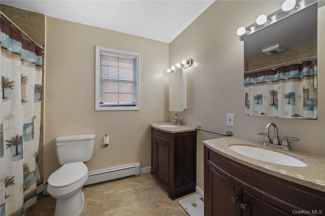 Bathroom featuring a shower with shower curtain, two vanities, and a baseboard radiator Bathroom featuring a shower with shower curtain, two vanities, and a baseboard radiator