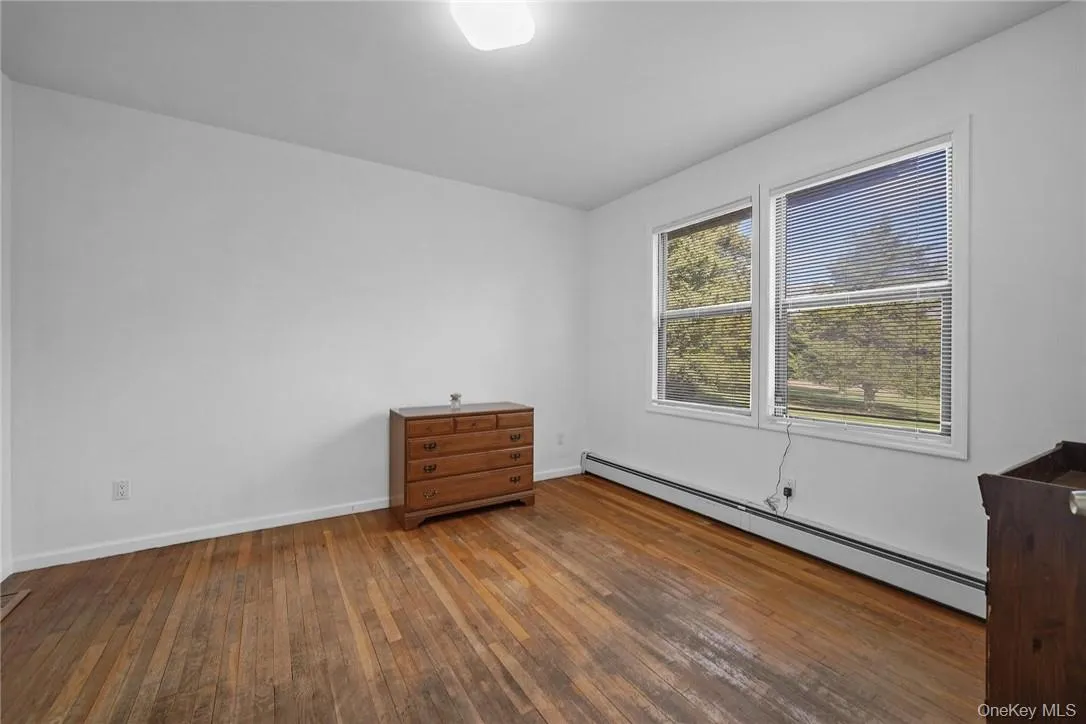 Unfurnished bedroom featuring a baseboard heating unit and hardwood / wood-style floors Unfurnished bedroom featuring a baseboard heating unit and hardwood / wood-style floors
