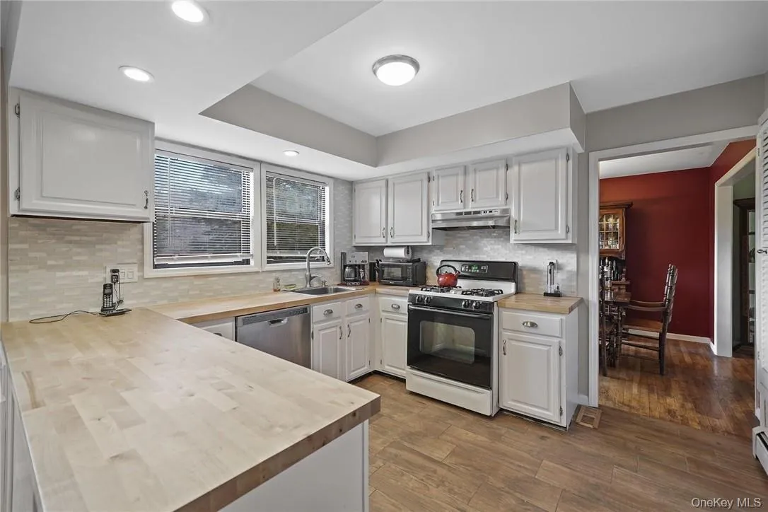 Kitchen featuring gas stove, white cabinetry, wood finished floors, stainless steel dishwasher, and under cabinet range hood Kitchen featuring gas stove, white cabinetry, wood finished floors, stainless steel dishwasher, and under cabinet range hood