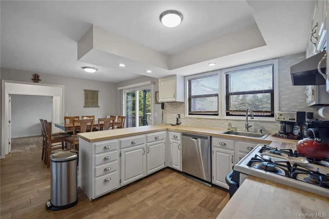 Kitchen featuring white cabinetry, light wood-type flooring, dishwasher, tasteful backsplash, and a peninsula Kitchen featuring white cabinetry, light wood-type flooring, dishwasher, tasteful backsplash, and a peninsula