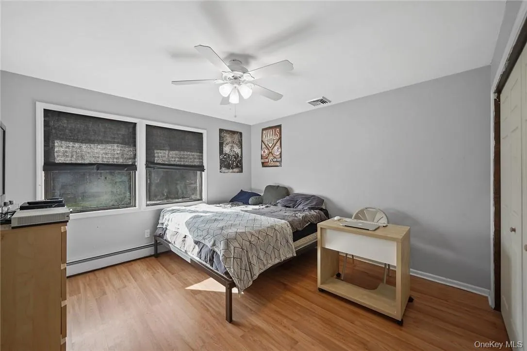 Bedroom featuring baseboard heating, a closet, light wood-style floors, and ceiling fan Bedroom featuring baseboard heating, a closet, light wood-style floors, and ceiling fan
