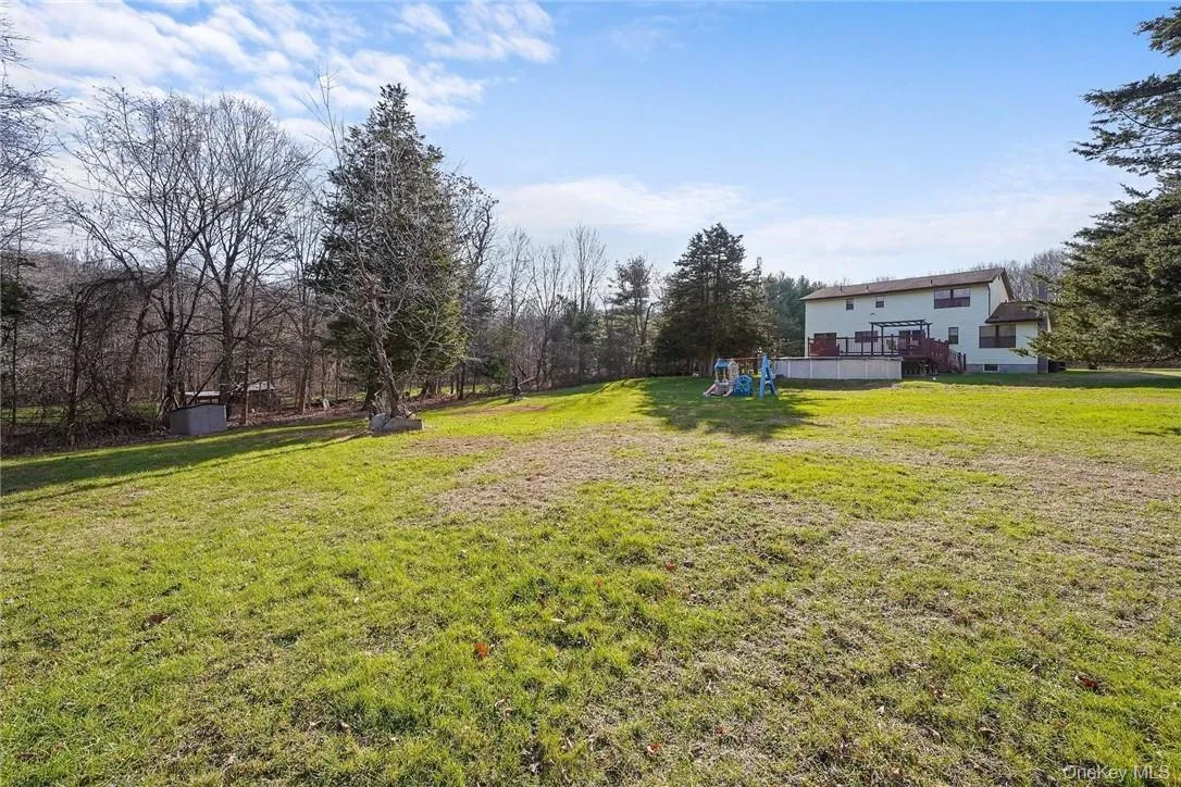 View of grassy yard with a deck, a playground, and view of scattered trees View of grassy yard with a deck, a playground, and view of scattered trees