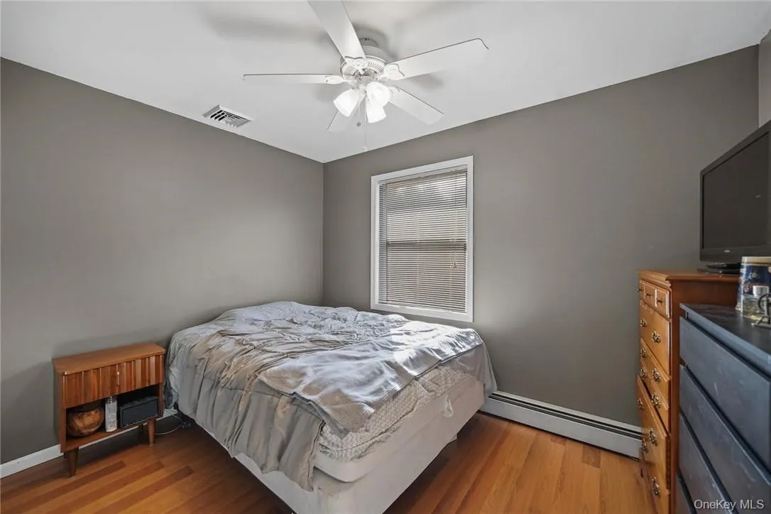 Bedroom featuring a baseboard heating unit, ceiling fan, and light wood-style floors Bedroom featuring a baseboard heating unit, ceiling fan, and light wood-style floors