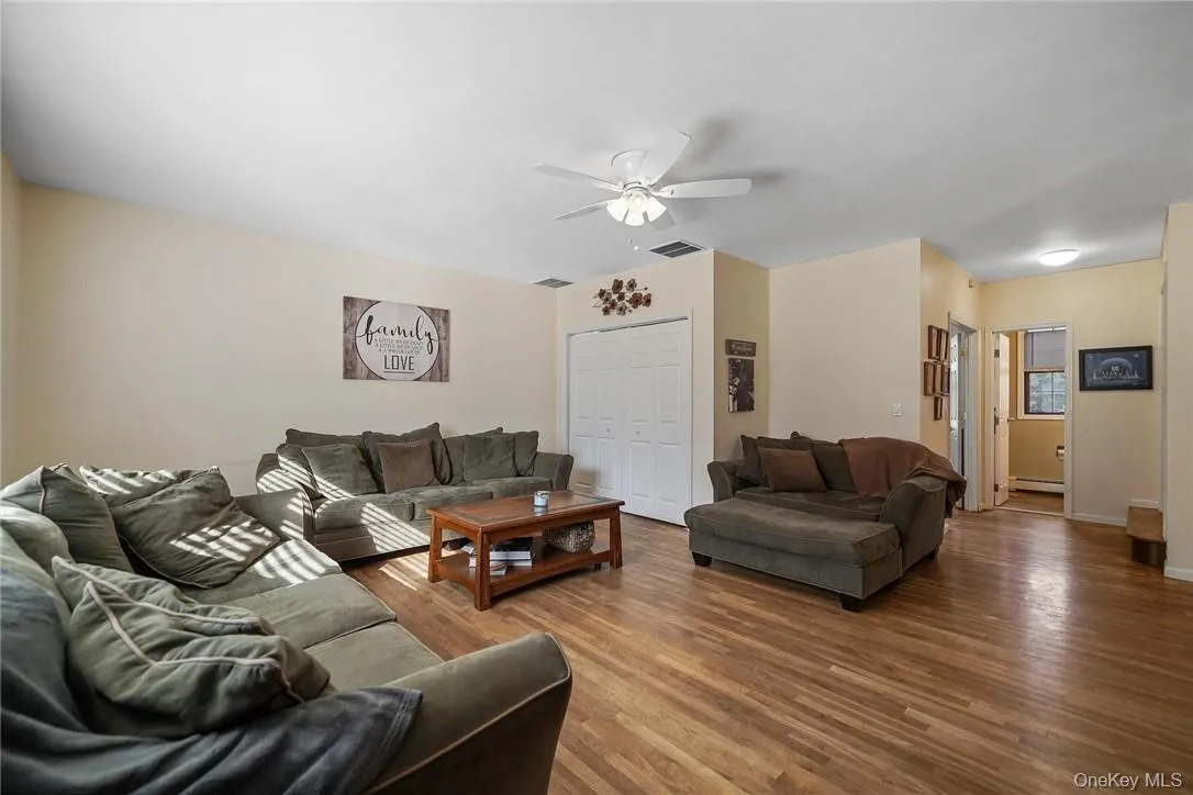 Living room with wood finished floors, a ceiling fan, and a baseboard heating unit Living room with wood finished floors, a ceiling fan, and a baseboard heating unit