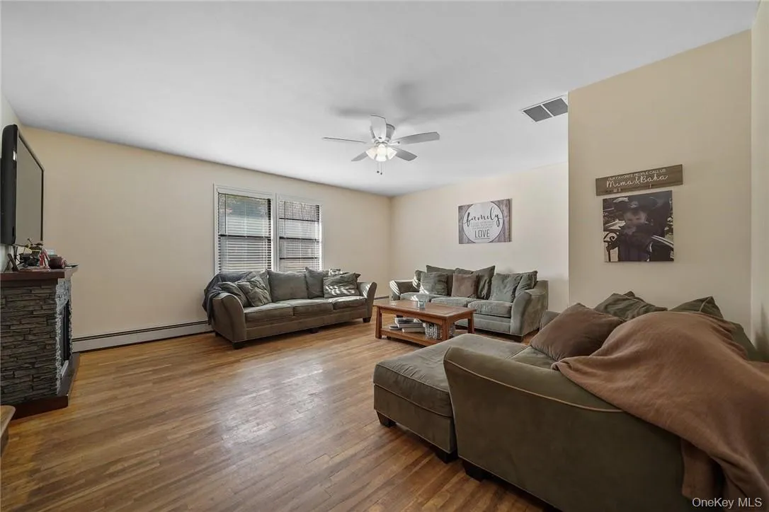Living area with baseboard heating, wood finished floors, ceiling fan, and a stone fireplace Living area with baseboard heating, wood finished floors, ceiling fan, and a stone fireplace