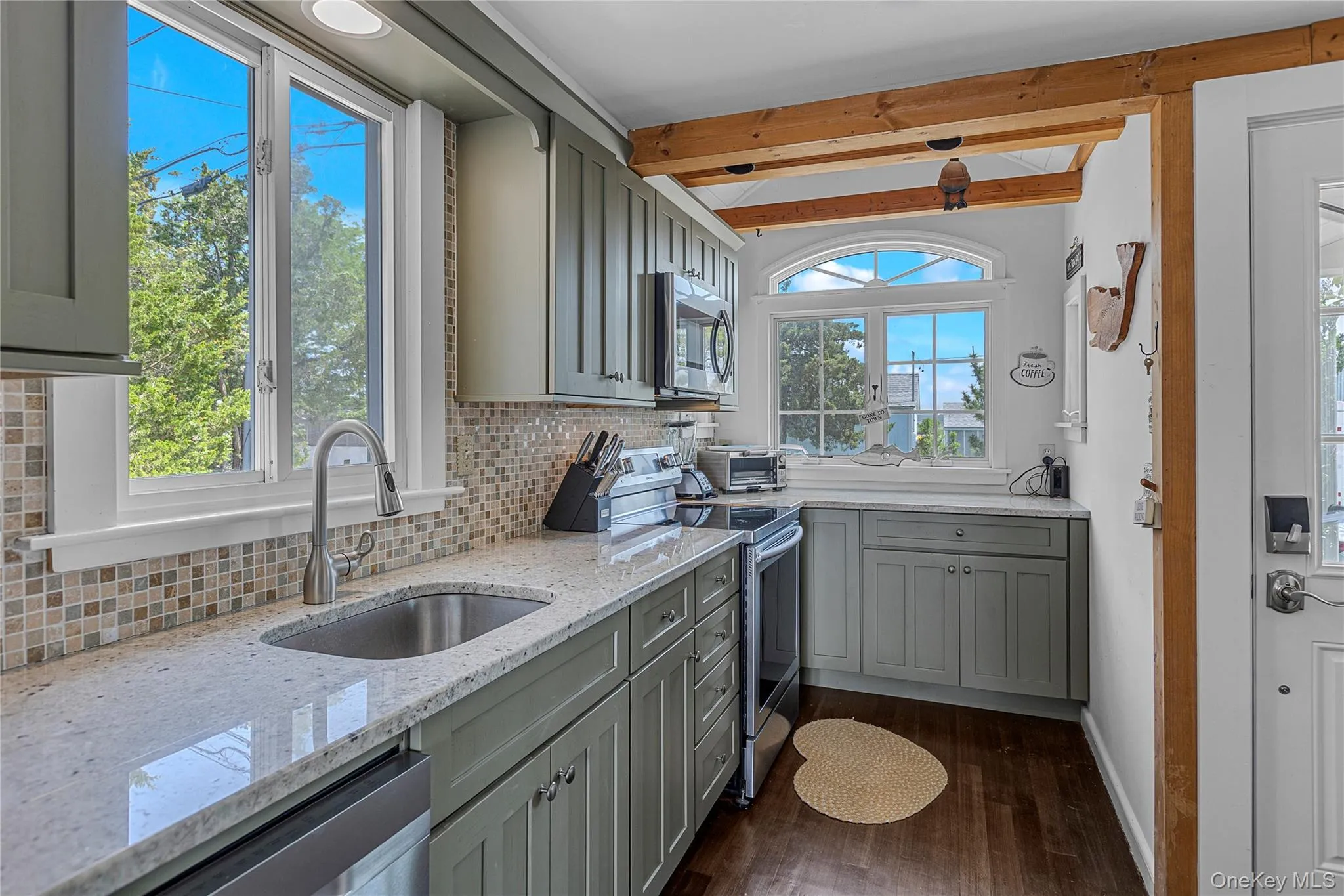 Kitchen with appliances with stainless steel finishes, gray cabinetry, dark wood finished floors, tasteful backsplash, and beam ceiling Kitchen with appliances with stainless steel finishes, gray cabinetry, dark wood finished floors, tasteful backsplash, and beam ceiling