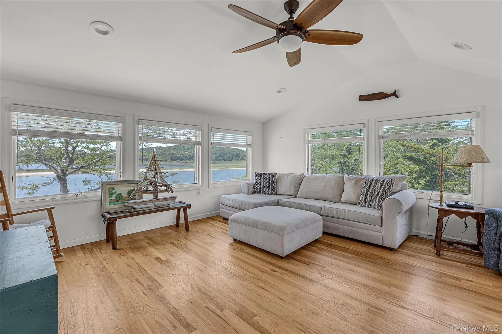 Living room with healthy amount of natural light, a ceiling fan, a water view, vaulted ceiling, and light wood-style floors Living room with healthy amount of natural light, a ceiling fan, a water view, vaulted ceiling, and light wood-style floors