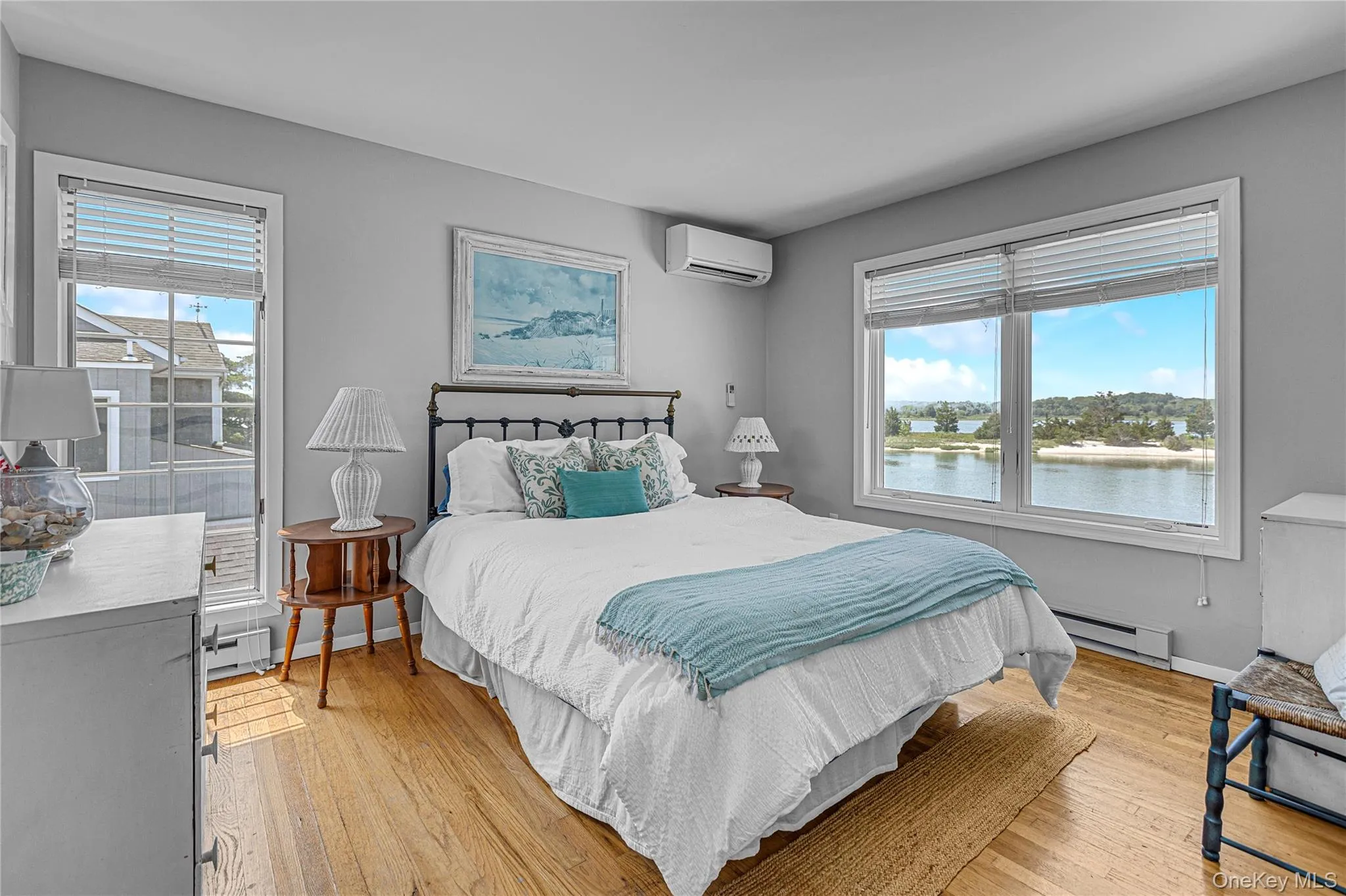 Bedroom featuring a wall mounted AC, multiple windows, light wood-type flooring, and a baseboard radiator Bedroom featuring a wall mounted AC, multiple windows, light wood-type flooring, and a baseboard radiator