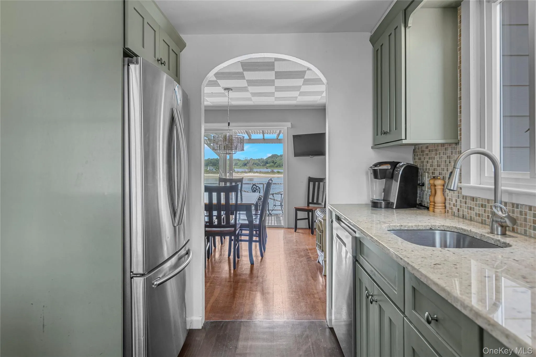 Kitchen featuring appliances with stainless steel finishes, light stone countertops, backsplash, green cabinets, and dark wood-type flooring Kitchen featuring appliances with stainless steel finishes, light stone countertops, backsplash, green cabinets, and dark wood-type flooring