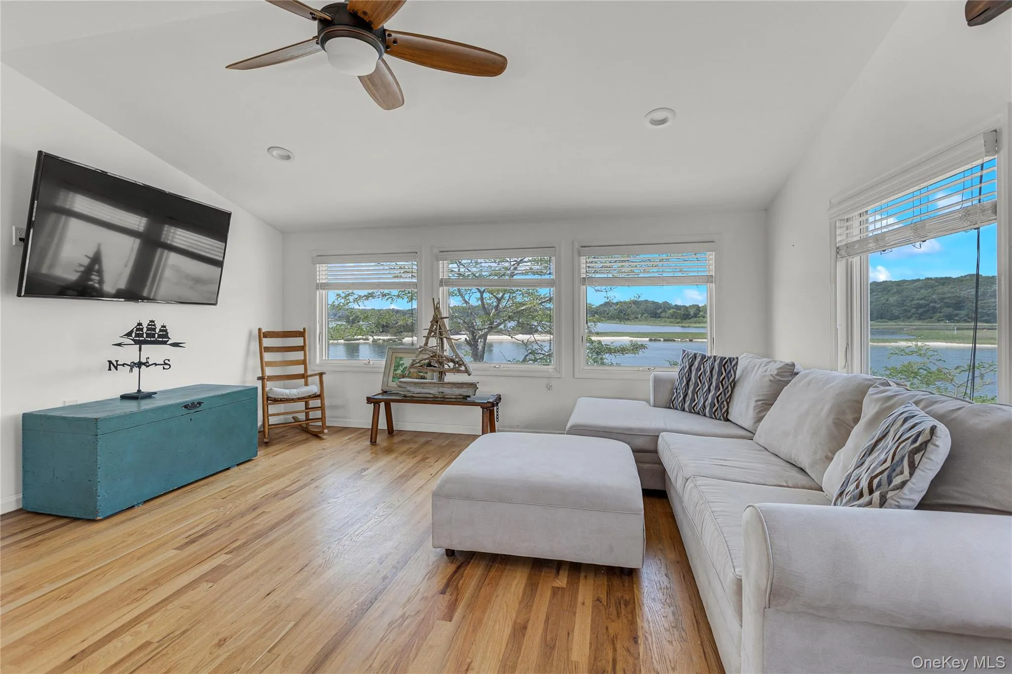 Living room with lofted ceiling, plenty of natural light, wood finished floors, ceiling fan, and a water view Living room with lofted ceiling, plenty of natural light, wood finished floors, ceiling fan, and a water view