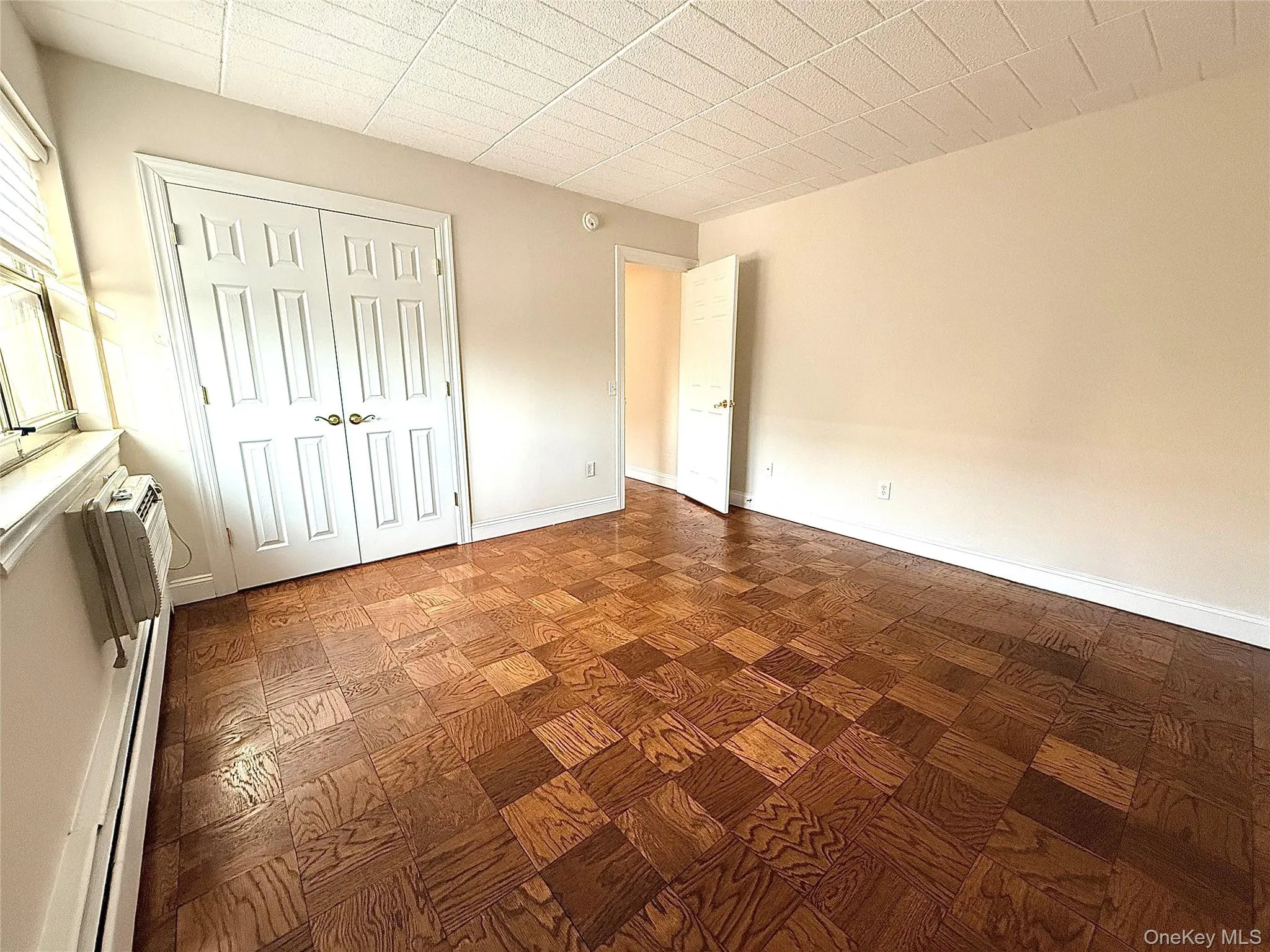 Primary bedroom with a large closet, a baseboard heating unit, parquet flooring, and an AC wall unit. Primary bedroom with a large closet, a baseboard heating unit, parquet flooring, and an AC wall unit.