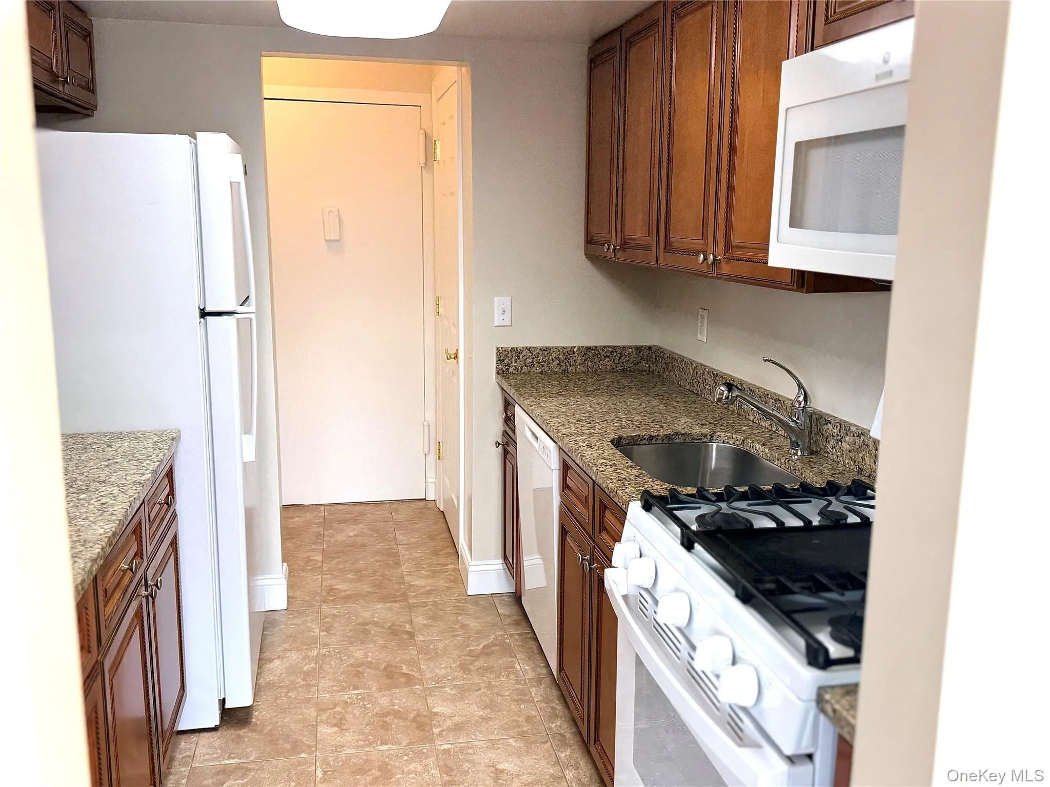 Kitchen with white appliances, dark stone counters, and brown cabinets Kitchen with white appliances, dark stone counters, and brown cabinets