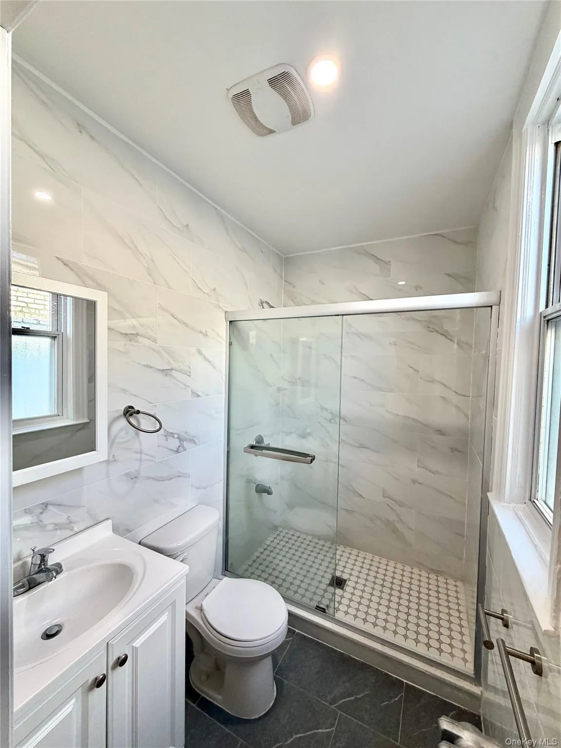 Bathroom featuring a marble finish shower, vanity, tile walls, and dark tile patterned floors Bathroom featuring a marble finish shower, vanity, tile walls, and dark tile patterned floors