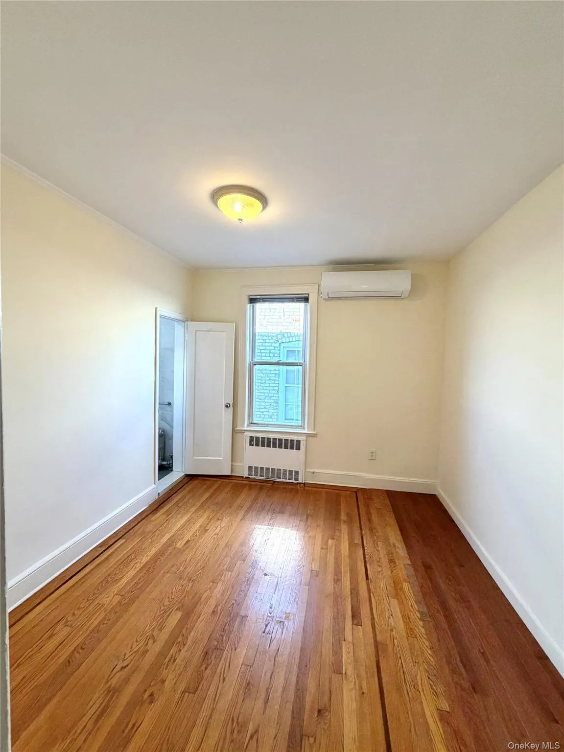 En-Suite bedroom featuring wood-type flooring, radiator, and a wall mounted air conditioner En-Suite bedroom featuring wood-type flooring, radiator, and a wall mounted air conditioner