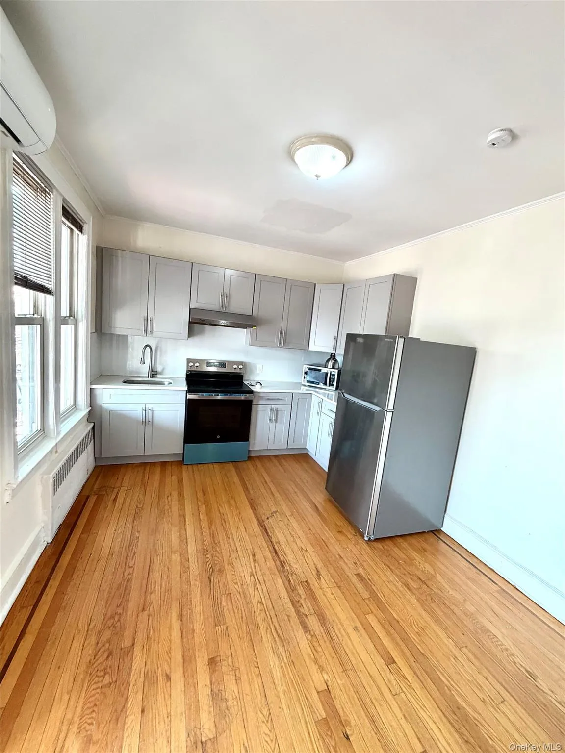 Kitchen with gray cabinetry, appliances with stainless steel finishes, light countertops, light wood-style flooring, and radiator Kitchen with gray cabinetry, appliances with stainless steel finishes, light countertops, light wood-style flooring, and radiator