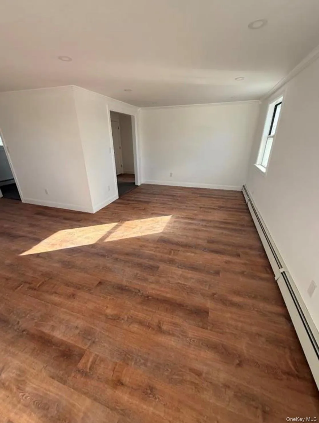 Unfurnished room with a baseboard radiator, crown molding, baseboards, and dark wood finished floors Unfurnished room with a baseboard radiator, crown molding, baseboards, and dark wood finished floors