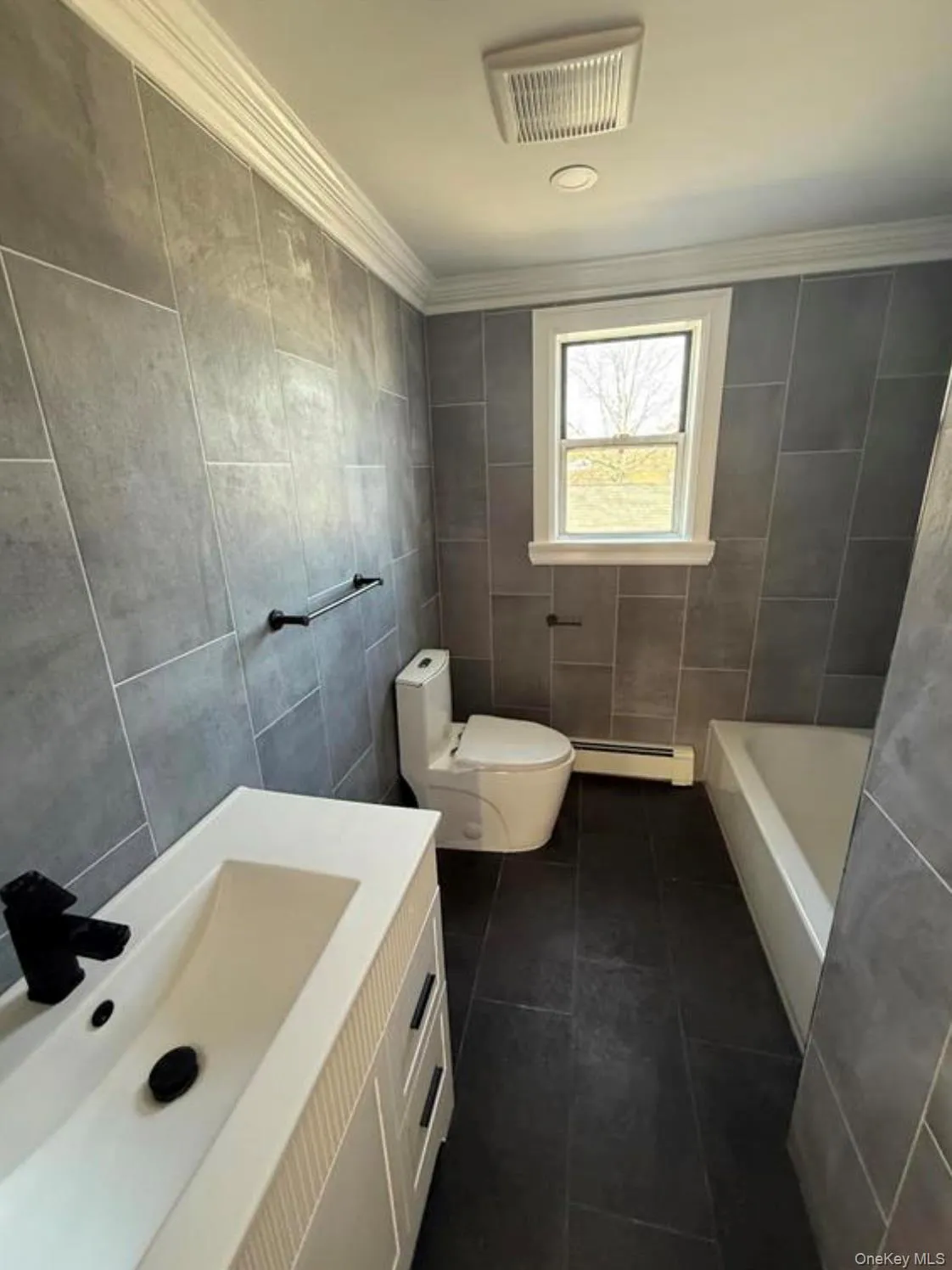 Bathroom with a baseboard radiator, tile patterned flooring, ornamental molding, toilet, and tile walls Bathroom with a baseboard radiator, tile patterned flooring, ornamental molding, toilet, and tile walls