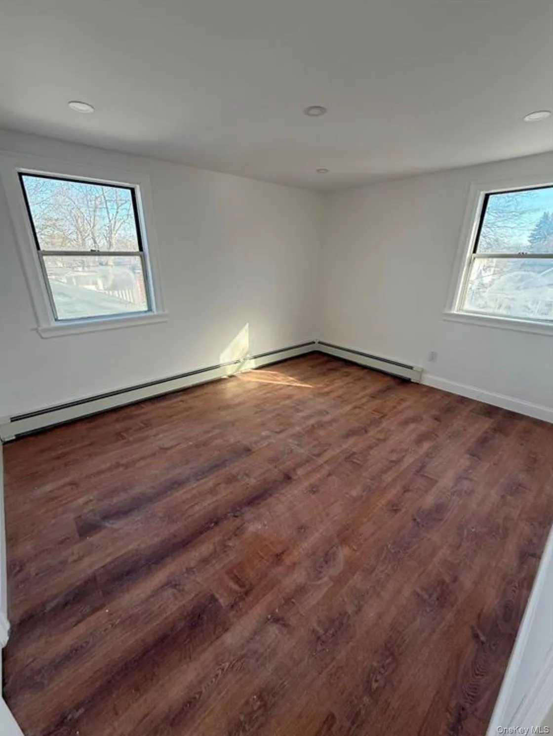 Unfurnished room featuring baseboard heating, dark wood-style flooring, recessed lighting, and baseboards Unfurnished room featuring baseboard heating, dark wood-style flooring, recessed lighting, and baseboards