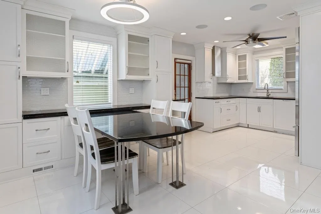 Kitchen with dark countertops, white cabinetry, light tile flooring, glass insert cabinets, and recessed lighting. Kitchen with dark countertops, white cabinetry, light tile flooring, glass insert cabinets, and recessed lighting.
