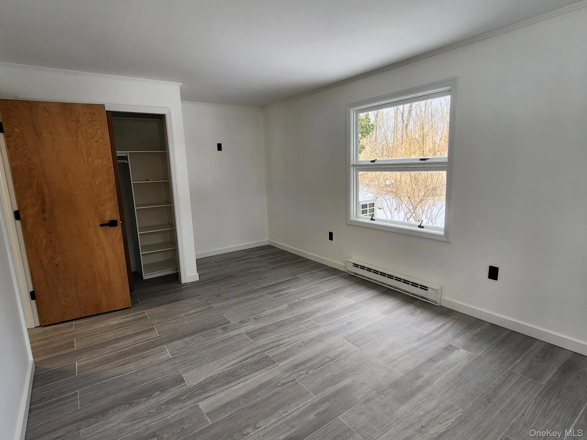 Unfurnished bedroom with light wood-type flooring, a baseboard heating unit, a closet, and ornamental molding Unfurnished bedroom with light wood-type flooring, a baseboard heating unit, a closet, and ornamental molding