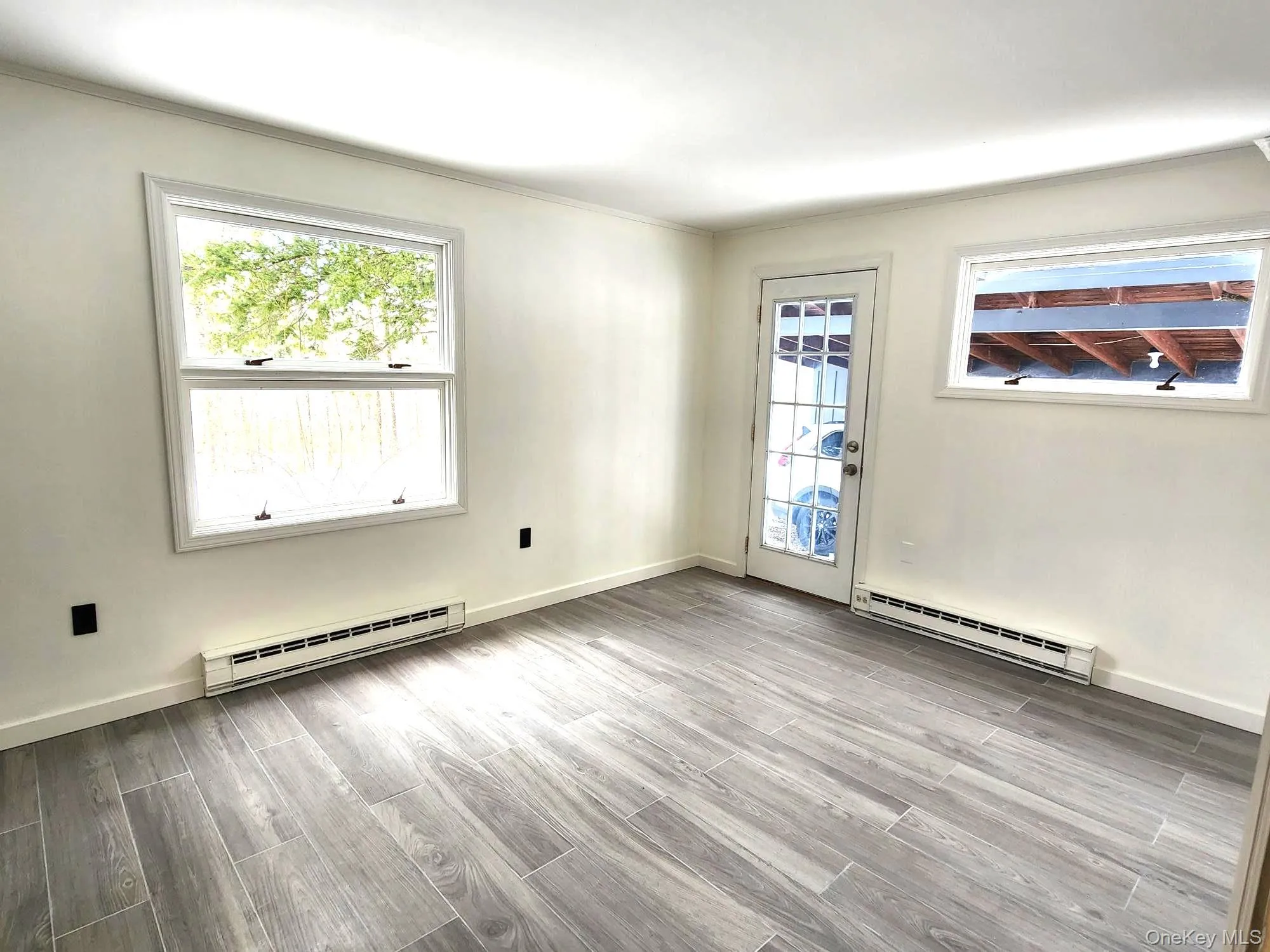 Unfurnished room featuring wood tiled floors, a baseboard radiator, and healthy amount of natural light Unfurnished room featuring wood tiled floors, a baseboard radiator, and healthy amount of natural light