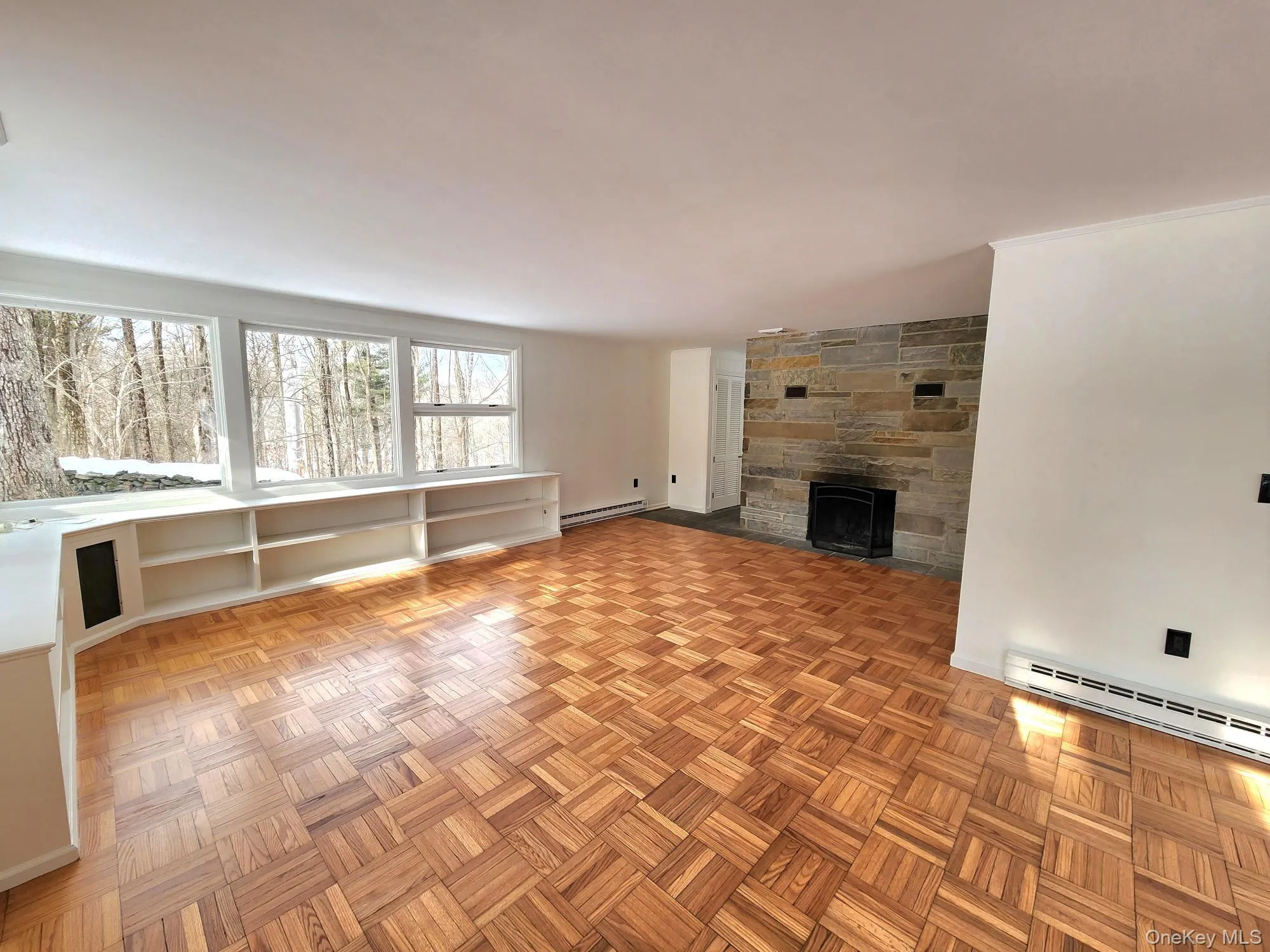 Unfurnished living room featuring a stone fireplace, parquet floors, a baseboard heating unit, and baseboard heating Unfurnished living room featuring a stone fireplace, parquet floors, a baseboard heating unit, and baseboard heating