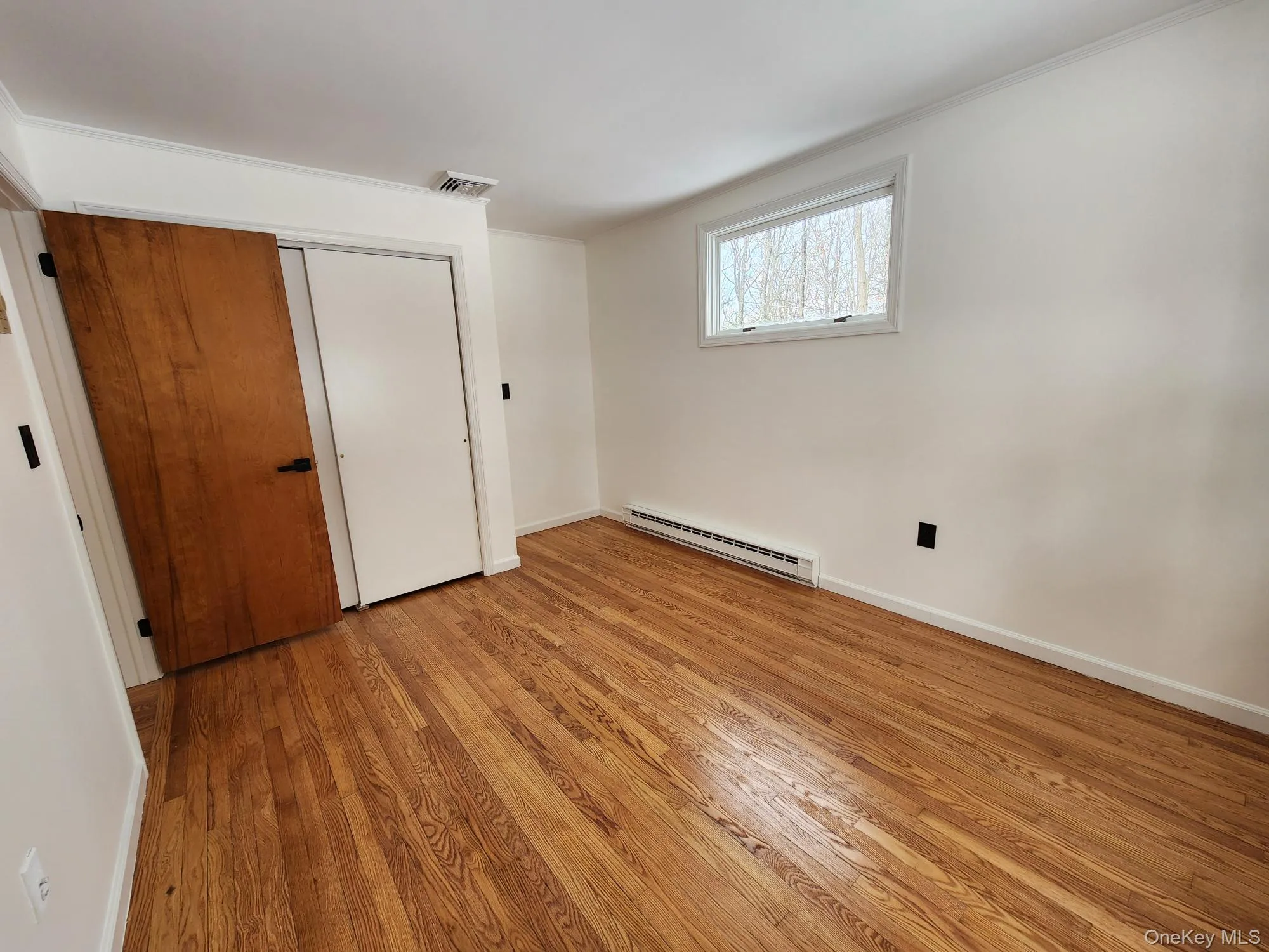 Unfurnished bedroom featuring light wood-style floors, a baseboard radiator, and a closet Unfurnished bedroom featuring light wood-style floors, a baseboard radiator, and a closet