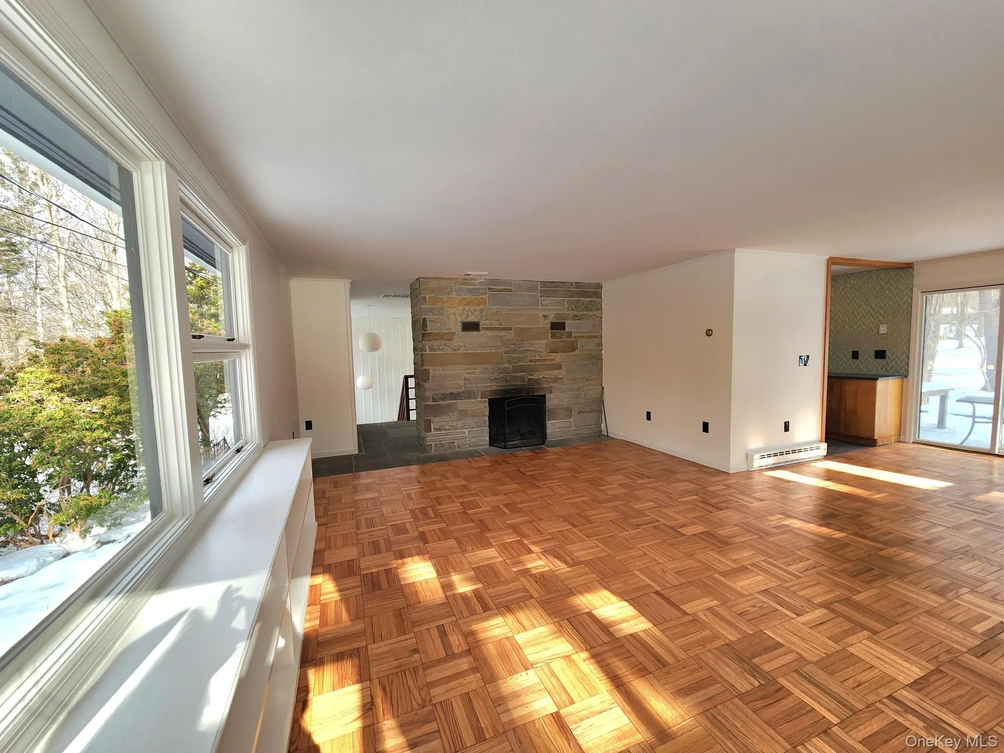 Unfurnished living room with a stone fireplace, parquet flooring, and baseboard heating Unfurnished living room with a stone fireplace, parquet flooring, and baseboard heating