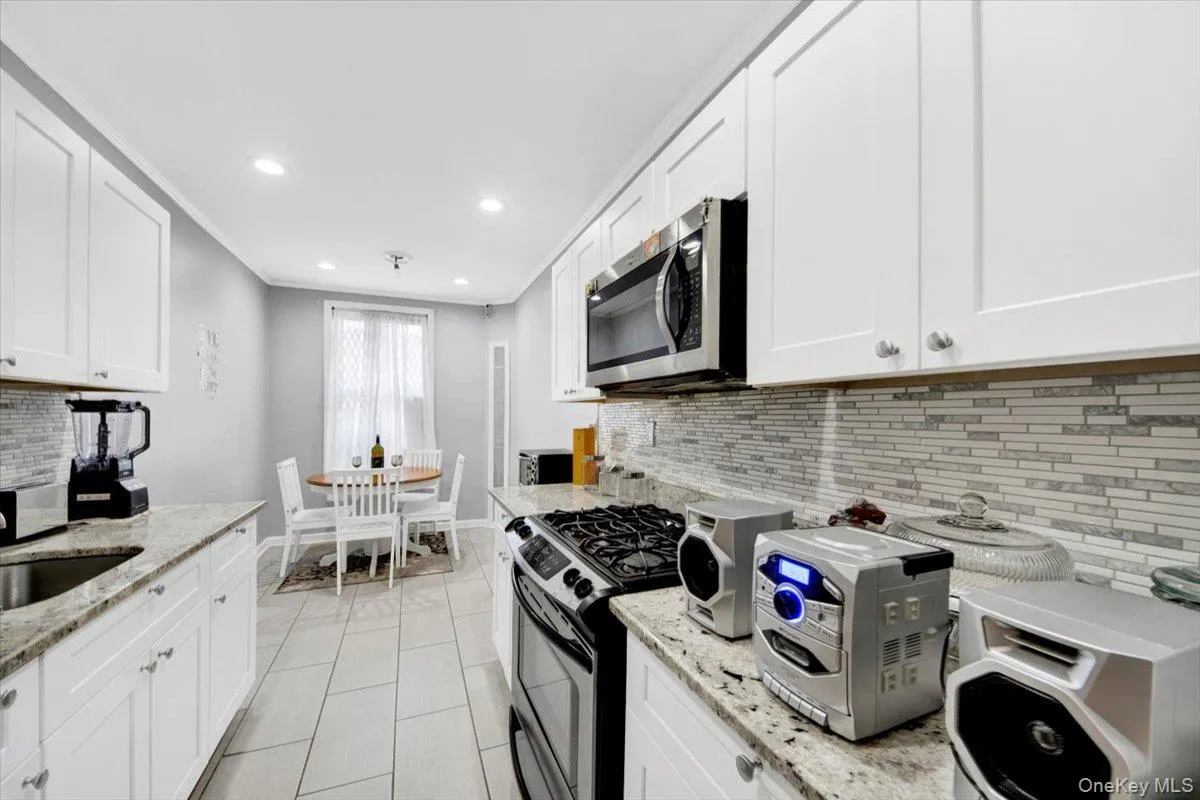 Kitchen with white cabinetry, light stone counters, stainless steel microwave, recessed lighting, and decorative backsplash Kitchen with white cabinetry, light stone counters, stainless steel microwave, recessed lighting, and decorative backsplash