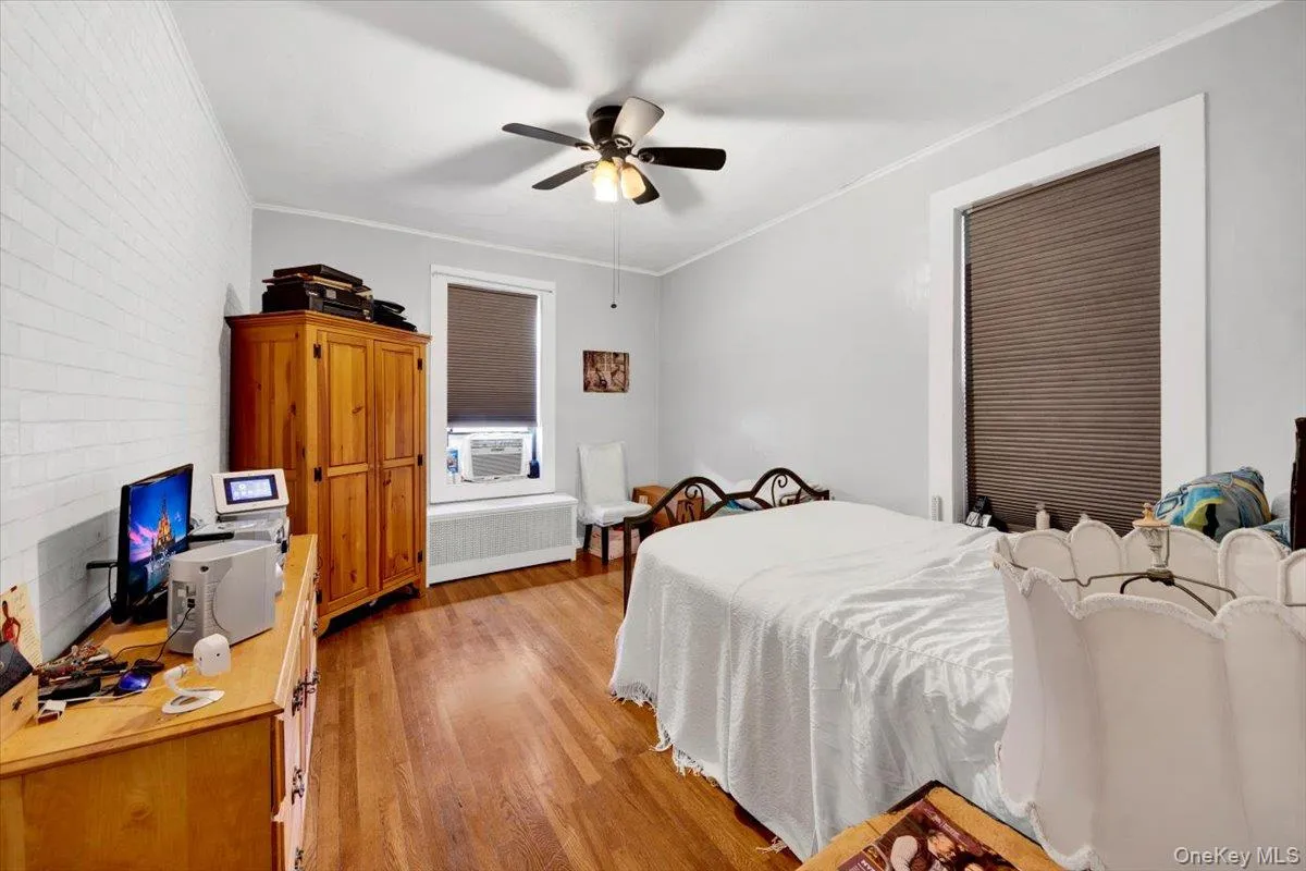 Bedroom featuring radiator, light wood-type flooring, crown molding, a ceiling fan, and an office area Bedroom featuring radiator, light wood-type flooring, crown molding, a ceiling fan, and an office area