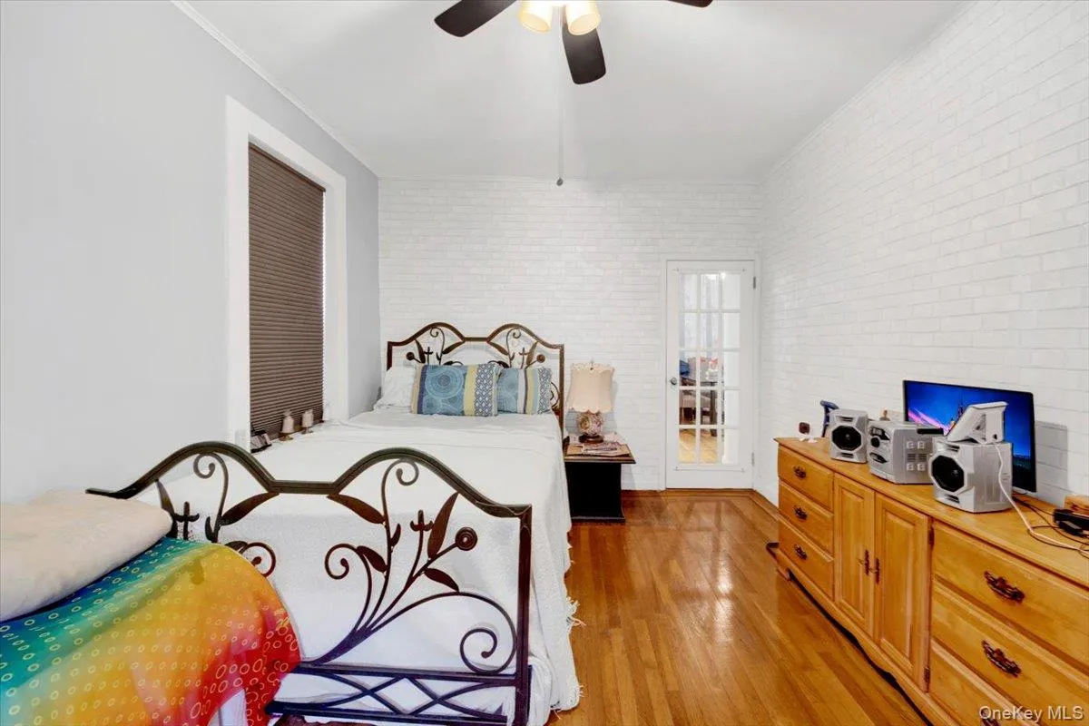 Bedroom featuring brick wall, light wood finished floors, ornamental molding, and a ceiling fan Bedroom featuring brick wall, light wood finished floors, ornamental molding, and a ceiling fan