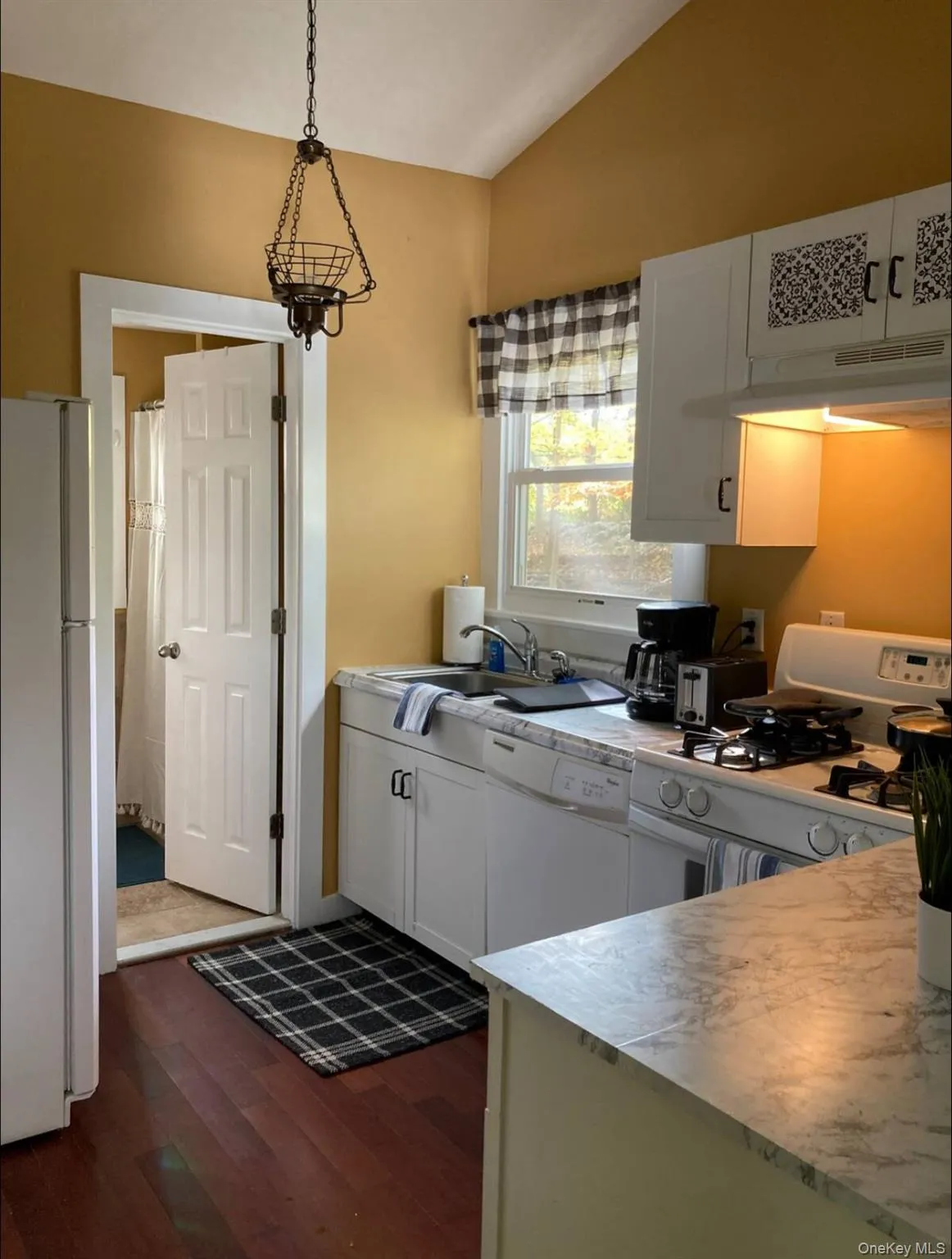 Kitchen featuring white appliances, white cabinets, light countertops, dark wood-type flooring, and lofted ceiling Kitchen featuring white appliances, white cabinets, light countertops, dark wood-type flooring, and lofted ceiling