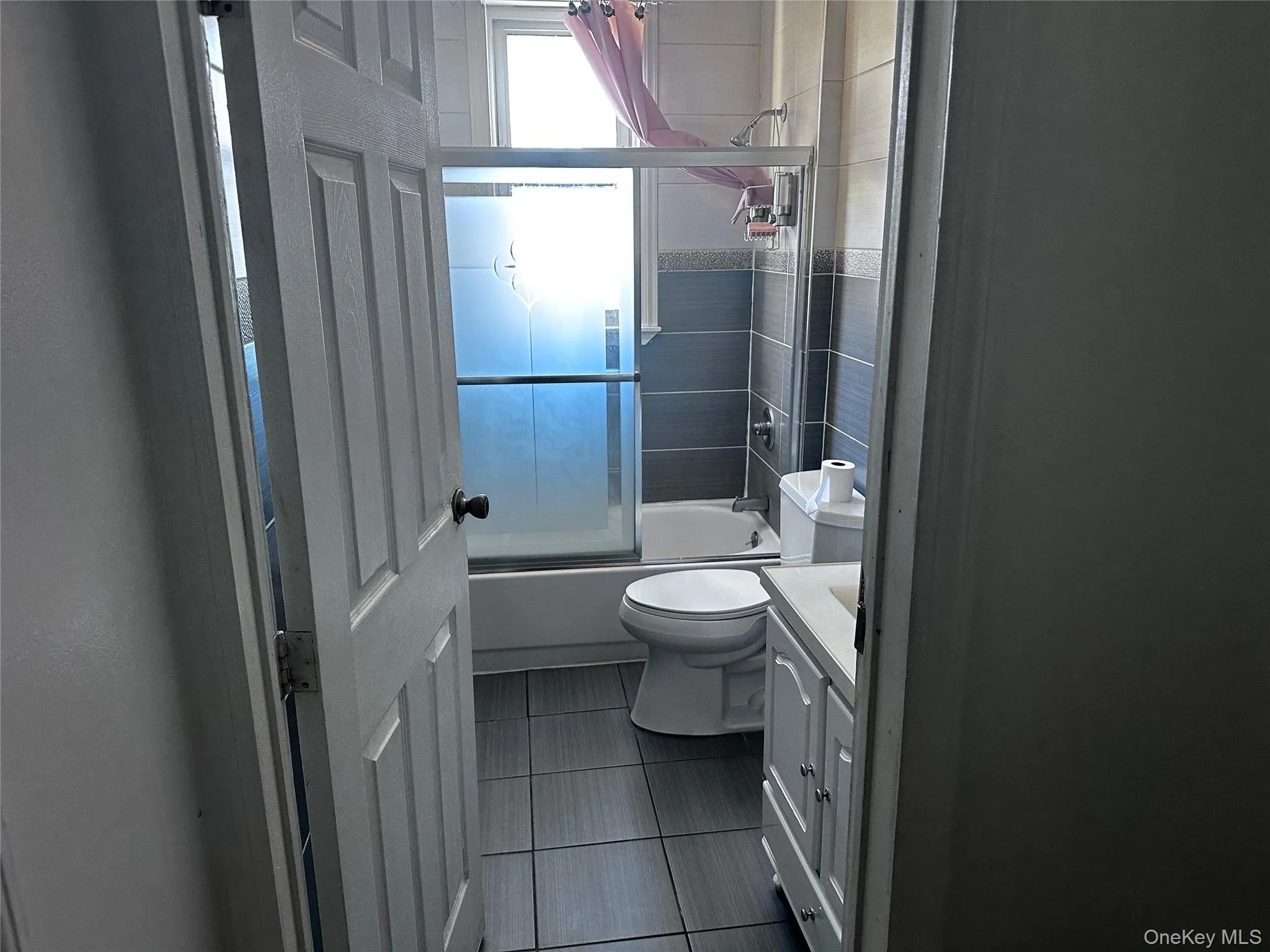 Full bath featuring combined bath / shower with glass door, vanity, and dark tile patterned floors Full bath featuring combined bath / shower with glass door, vanity, and dark tile patterned floors