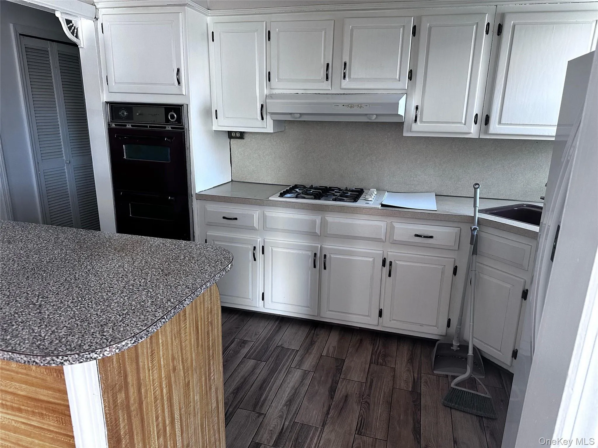 Kitchen featuring white cabinets, dark wood finished floors, under cabinet range hood, and white gas cooktop Kitchen featuring white cabinets, dark wood finished floors, under cabinet range hood, and white gas cooktop