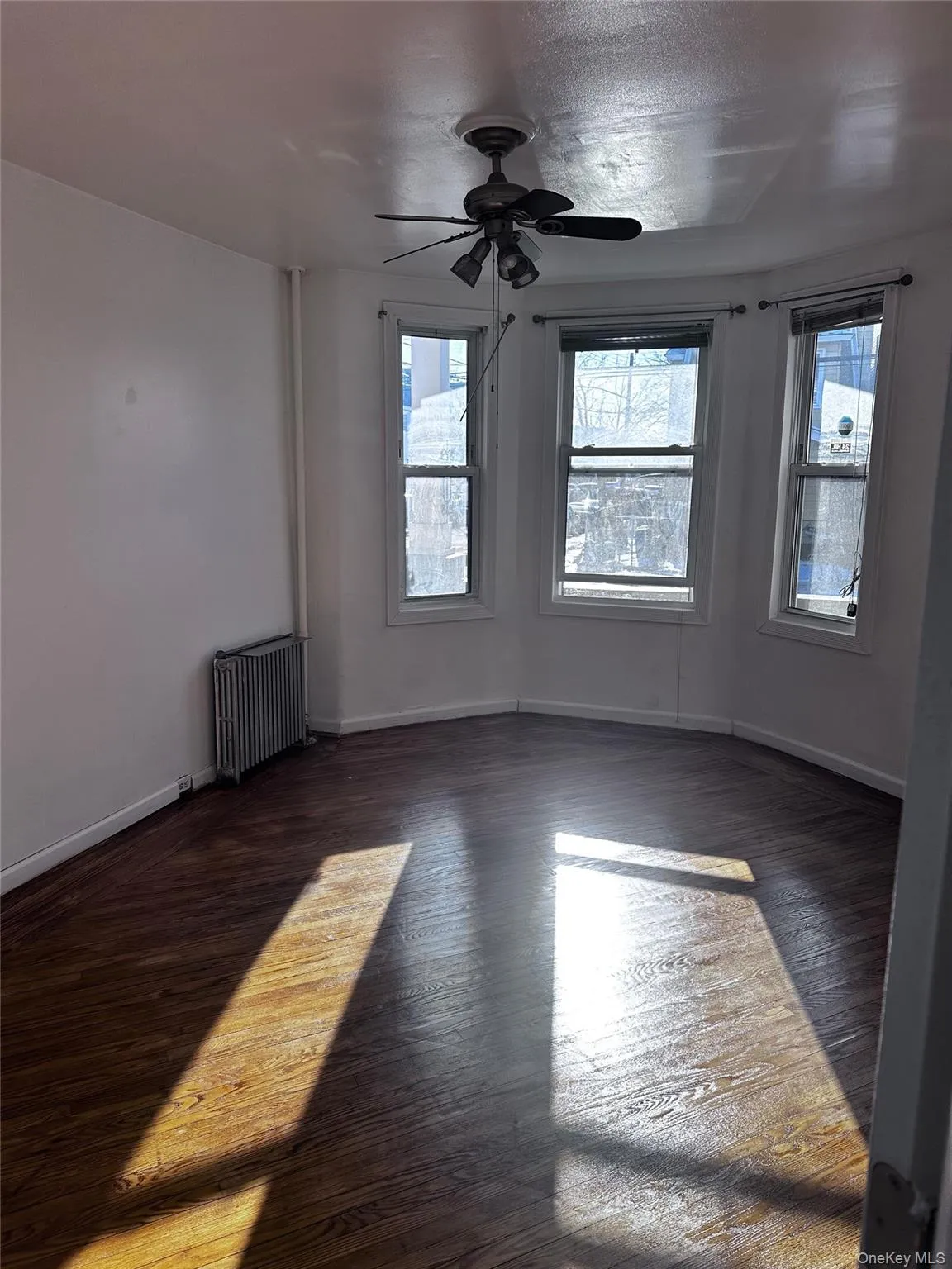 Spare room with dark wood-style flooring, radiator, a ceiling fan, and plenty of natural light Spare room with dark wood-style flooring, radiator, a ceiling fan, and plenty of natural light