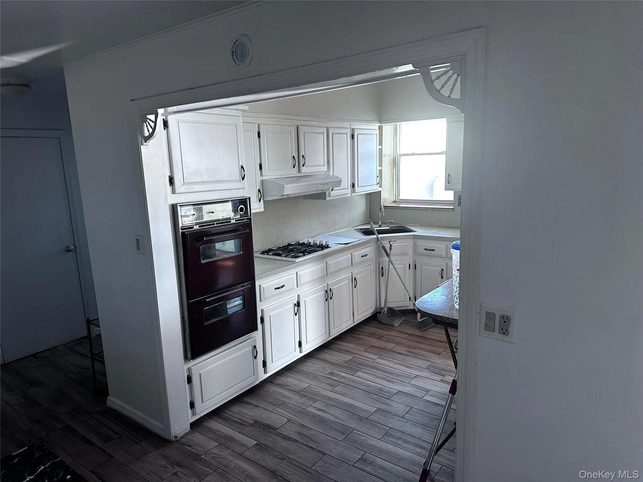 Kitchen with white cabinetry, light countertops, dark wood-style flooring, and under cabinet range hood Kitchen with white cabinetry, light countertops, dark wood-style flooring, and under cabinet range hood