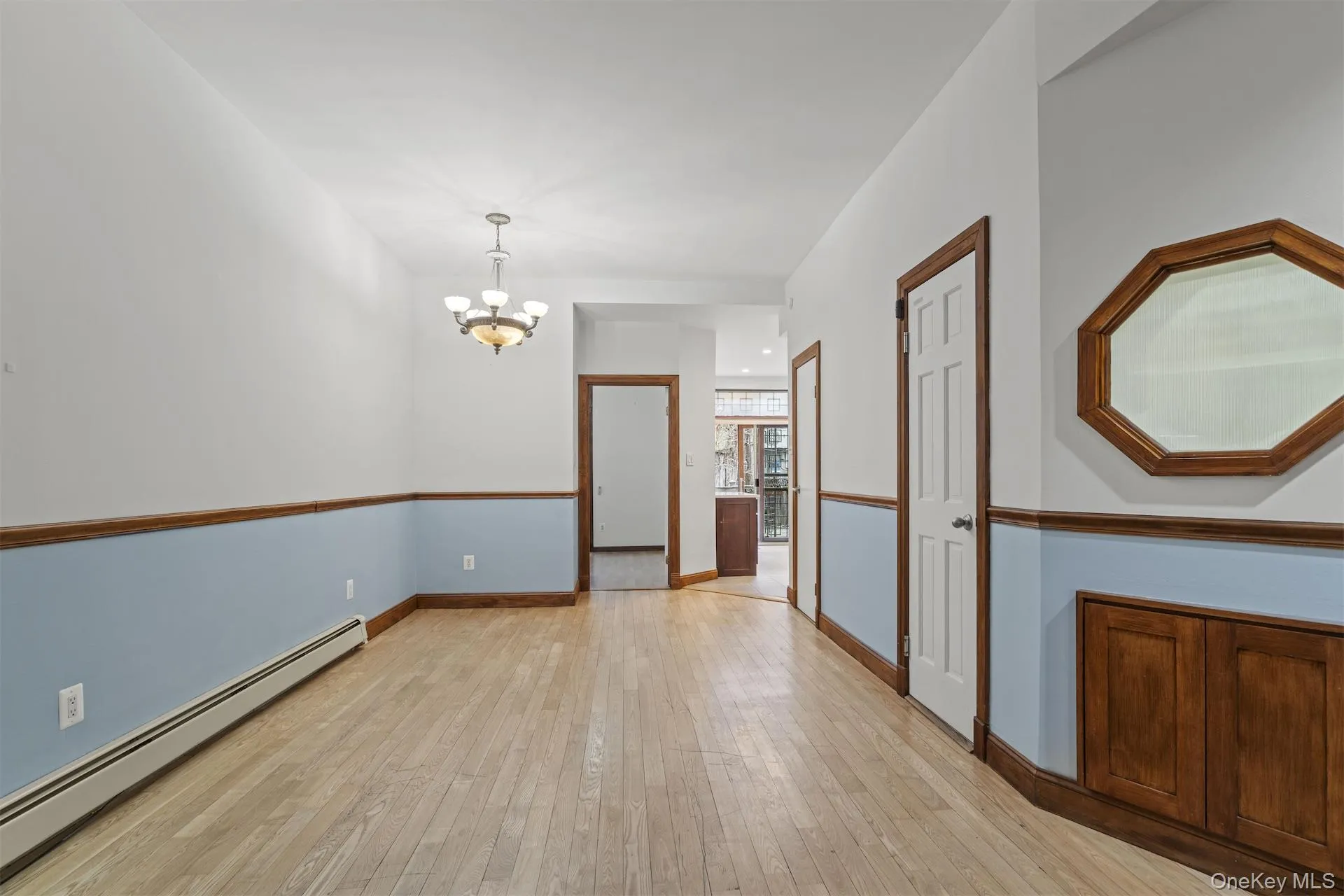 Empty room with a baseboard radiator, light wood-type flooring, and a chandelier Empty room with a baseboard radiator, light wood-type flooring, and a chandelier